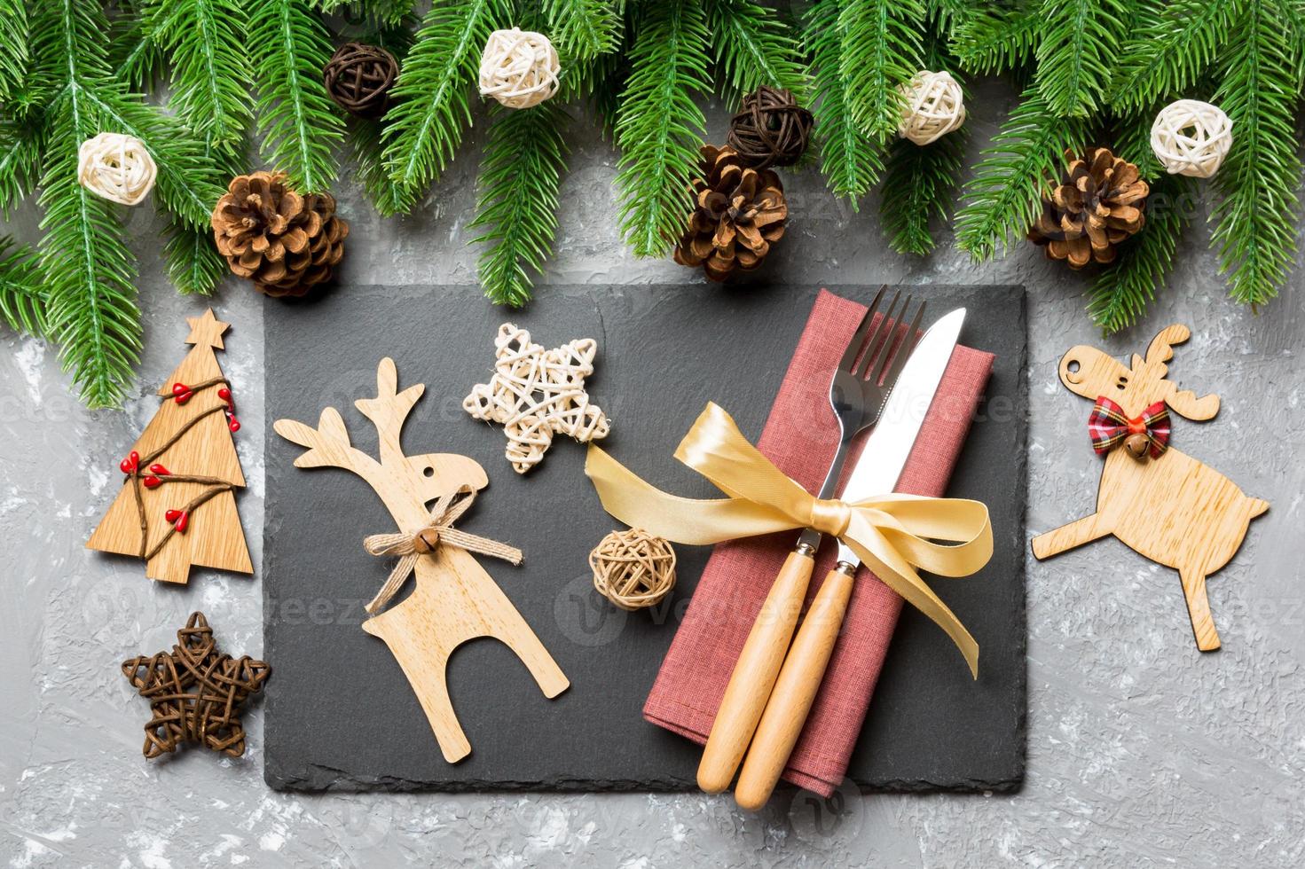 Top view of New Year dinner on festive cement background. Composition of plate, fork, knife, fir tree and decorations. Merry Christmas concept photo