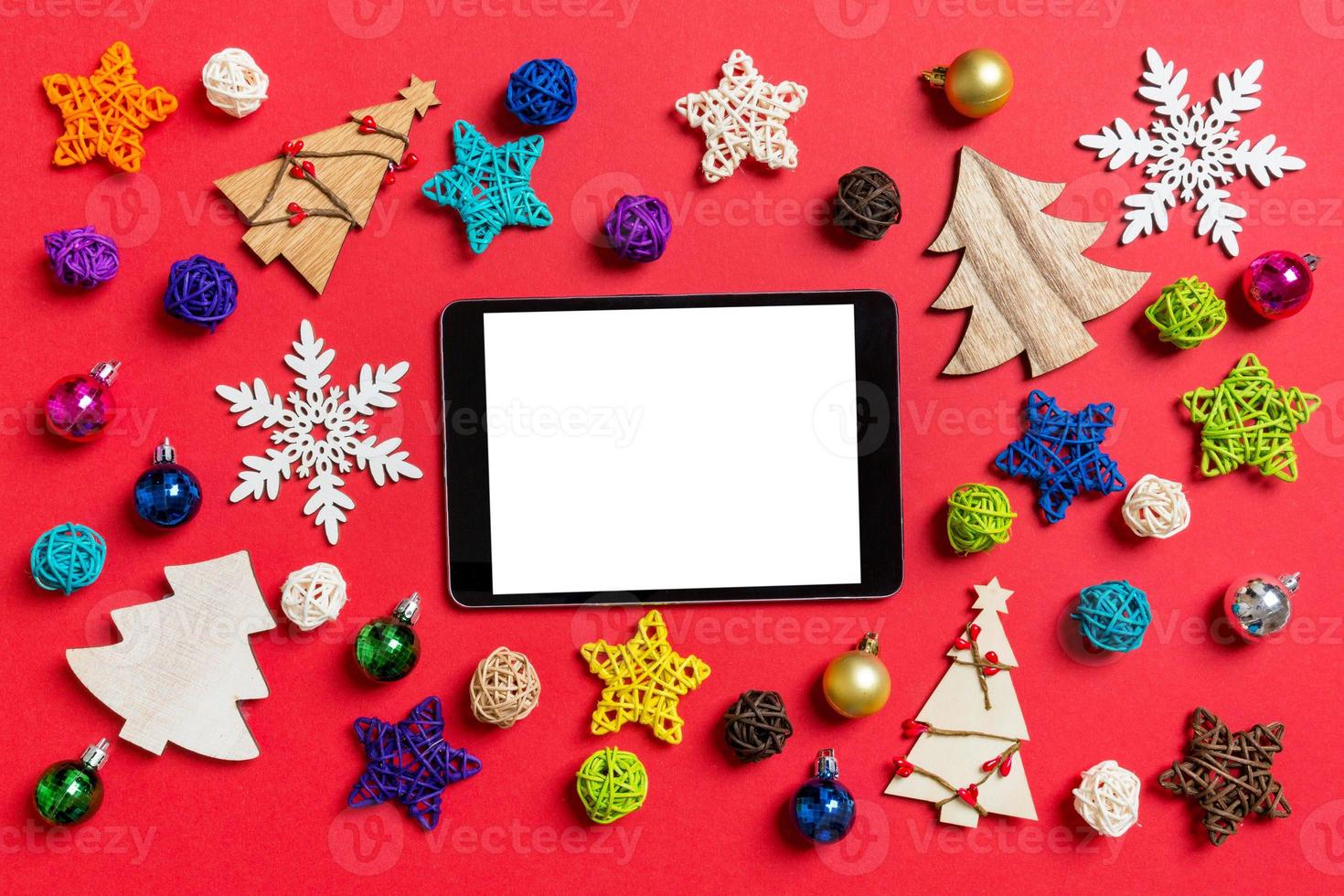 Top view of digital tablet on red background made of holiday decorations and toys. Christmas ornament concept photo