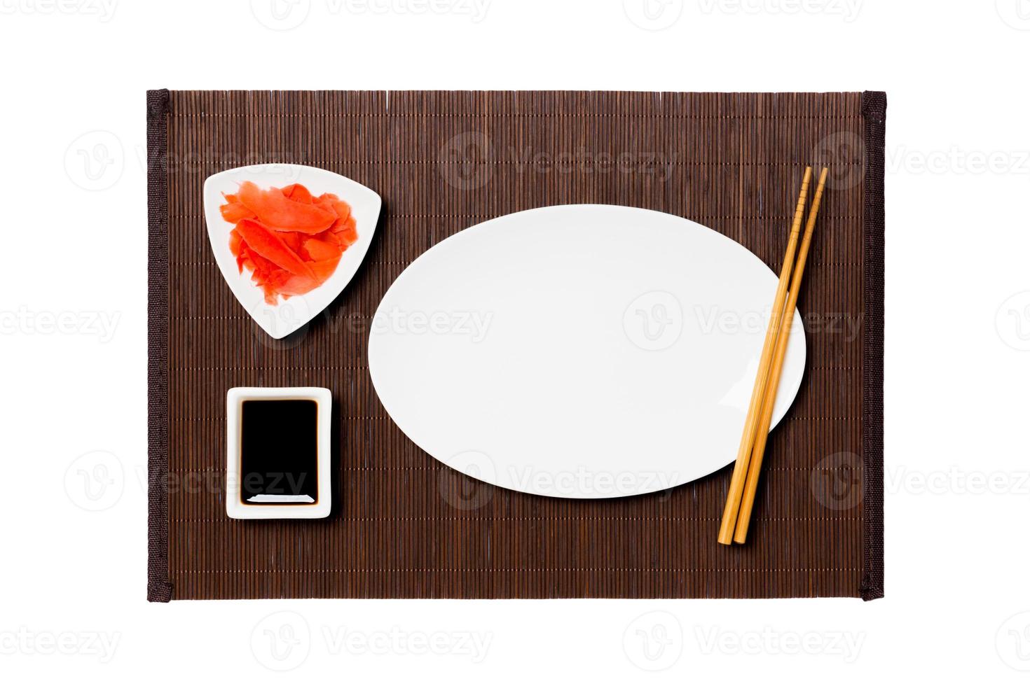 plato blanco ovalado vacío con palillos para sushi, jengibre y salsa de soja sobre fondo de estera de bambú oscuro. vista superior con espacio de copia para su diseño foto
