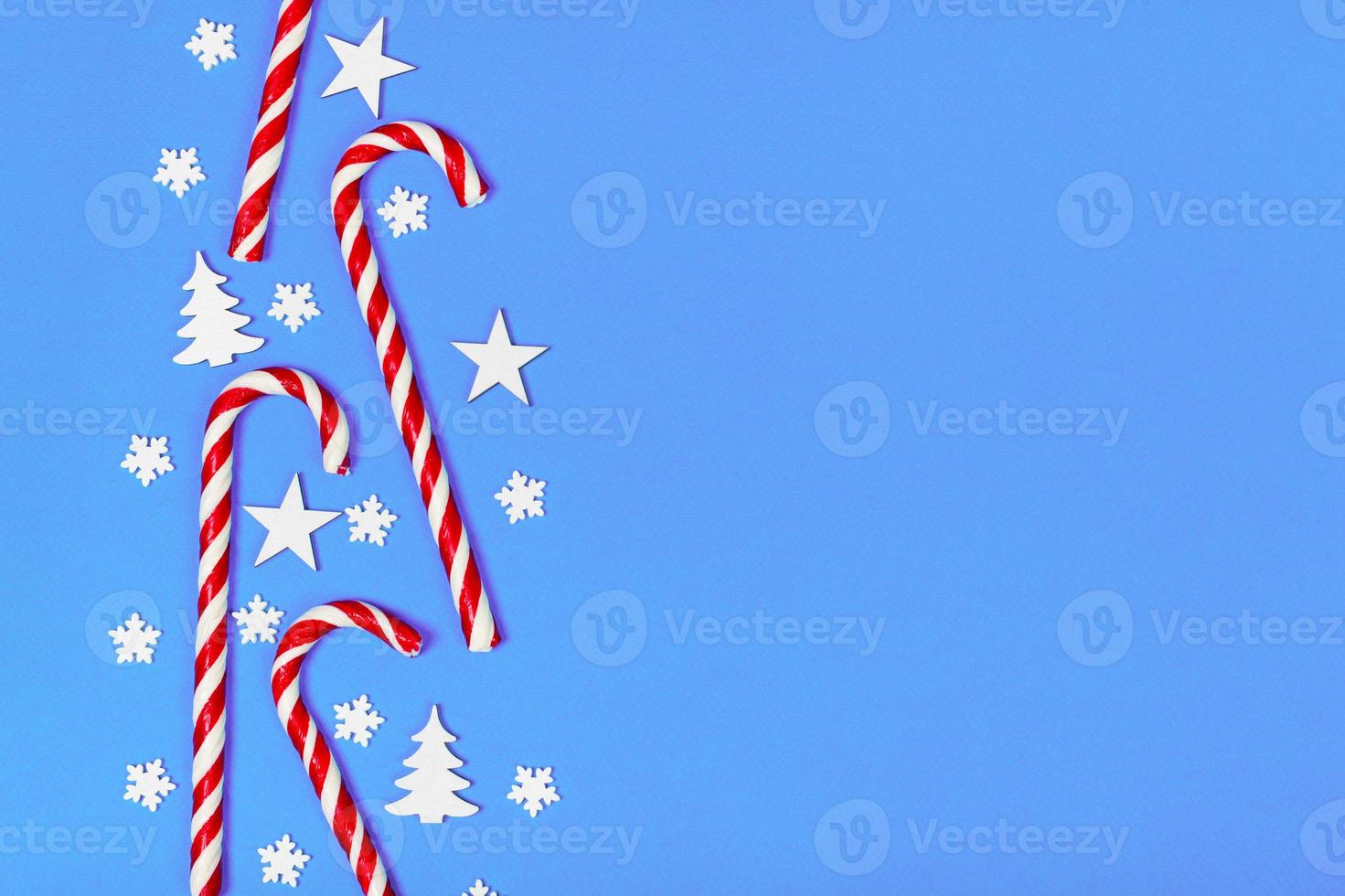 Christmas candy cane lied evenly in row on blue background with decorative snowflake and star. Flat lay and top view photo