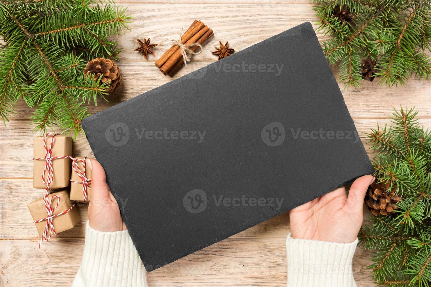 Famale hand hold Black slate round stone on wooden background with christmas decoration. top view, copy space. New Year concept photo