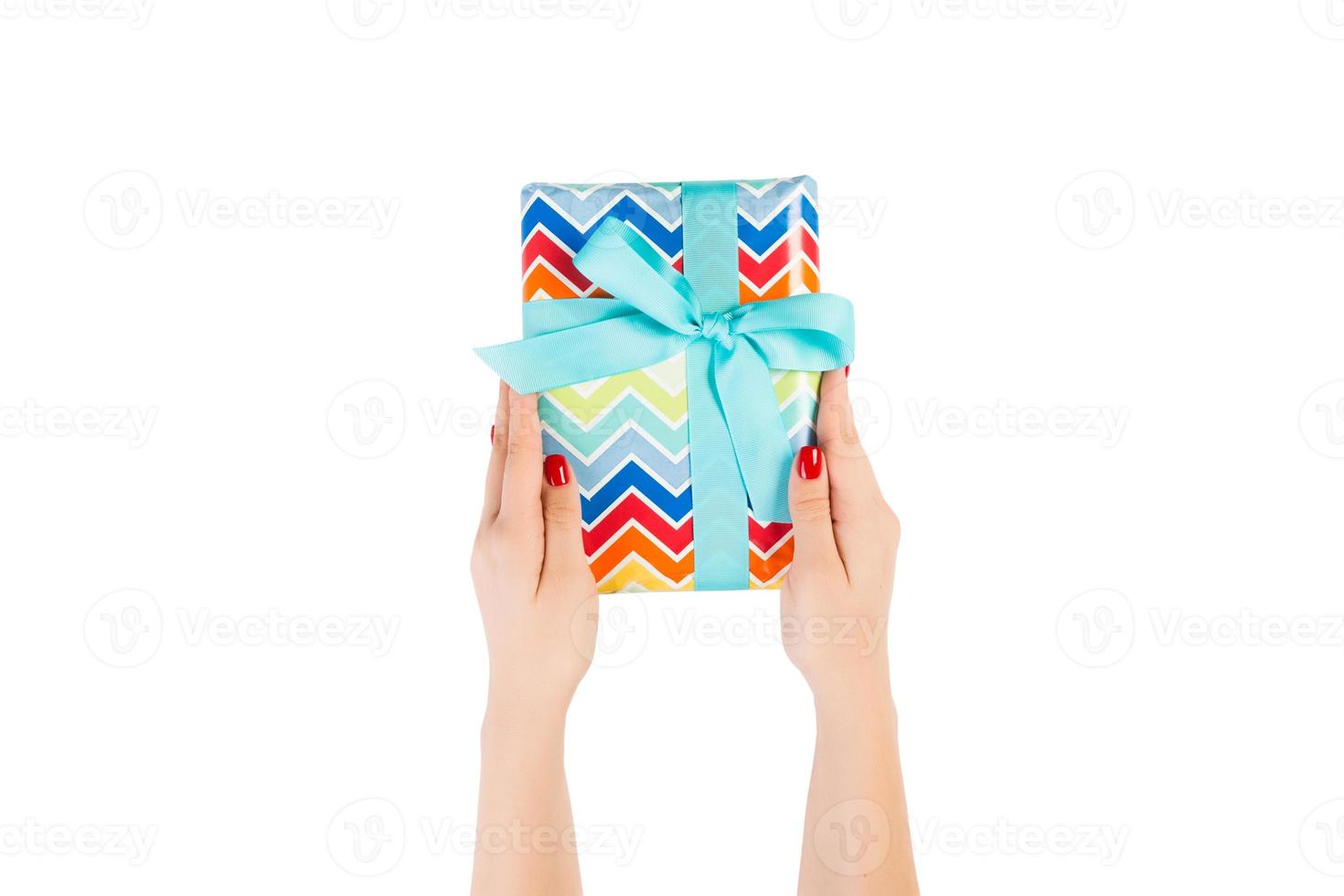 Woman hands give wrapped Christmas or other holiday handmade present in colored paper with blue ribbon. Isolated on white background, top view. thanksgiving Gift box concept photo