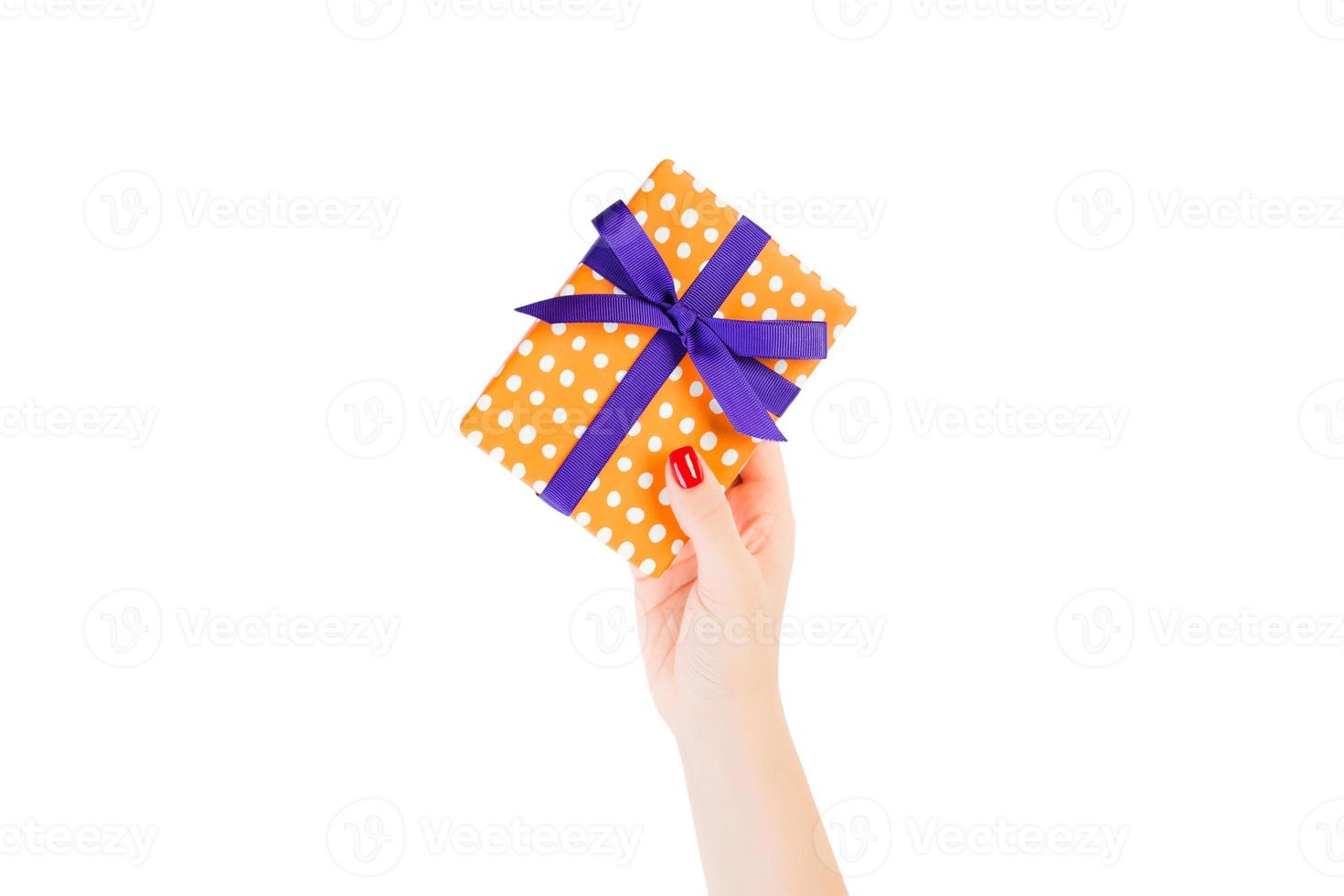 las manos de las mujeres dan Navidad envuelta u otro regalo hecho a mano en papel naranja con cinta morada. aislado sobre fondo blanco, vista superior. concepto de caja de regalo de acción de gracias foto