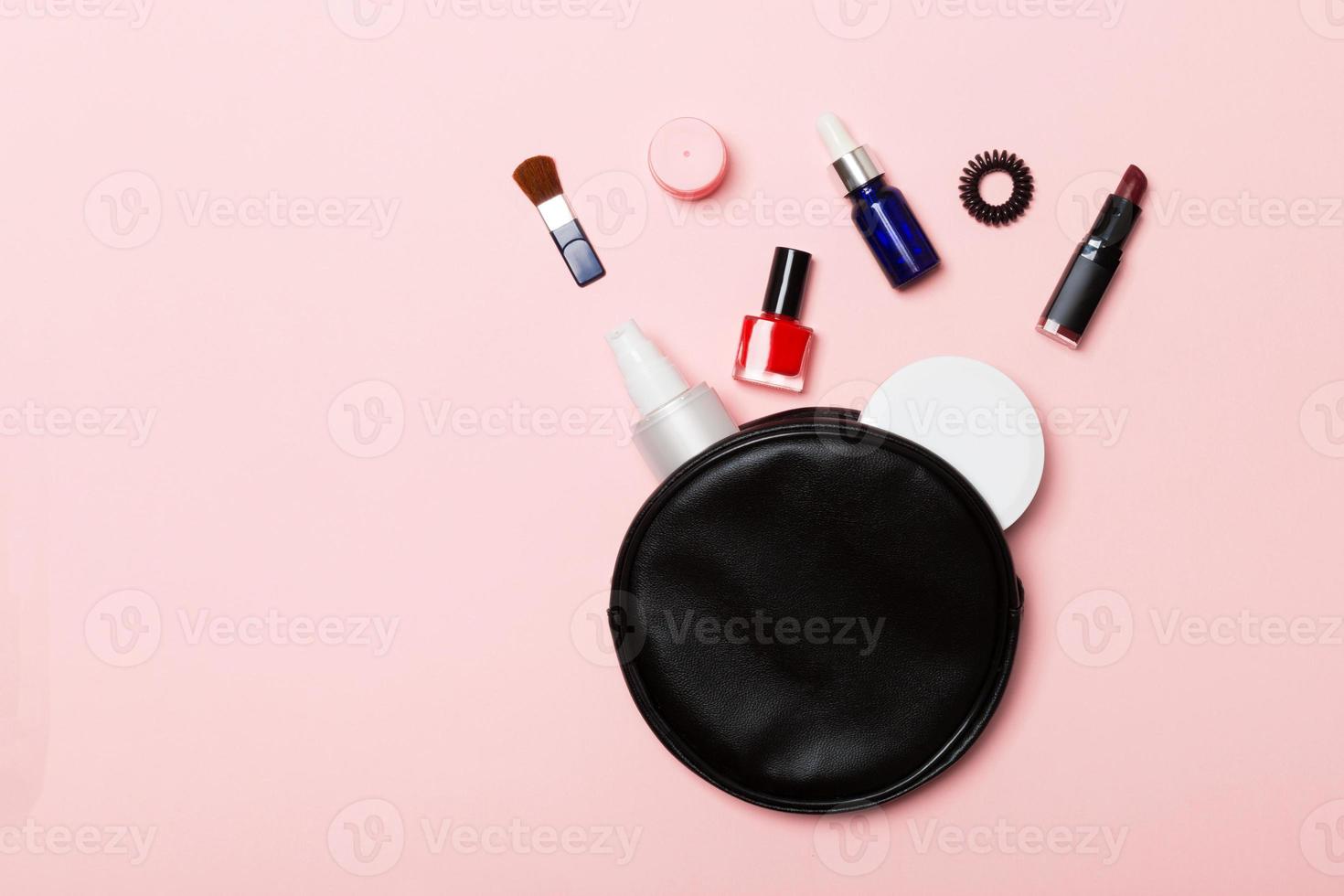 Top view of set of make up and skin care products spilling out of cosmetics bag on pink background. Beauty concept photo