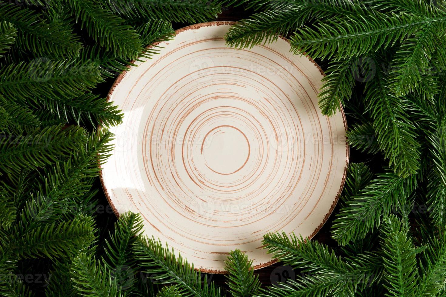 Top view of white plate surrounded with fir tree branches. Christmas dinner concept with copy space photo
