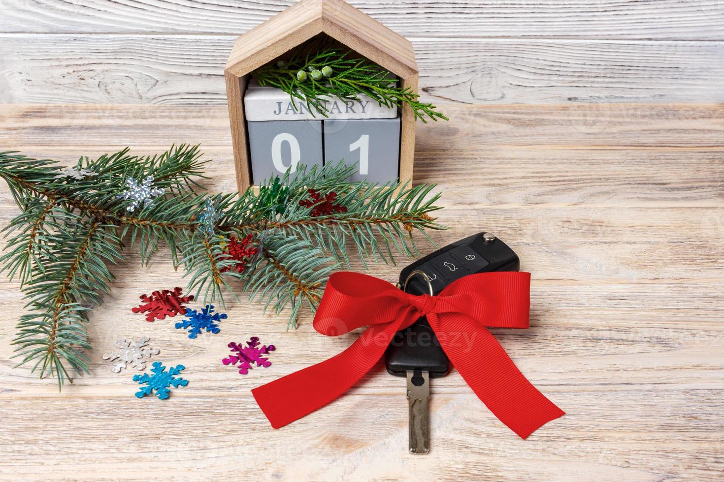 llave de coche con lazo colorido y calendario, árbol de navidad, ramas, copos de nieve, sobre fondo de madera foto