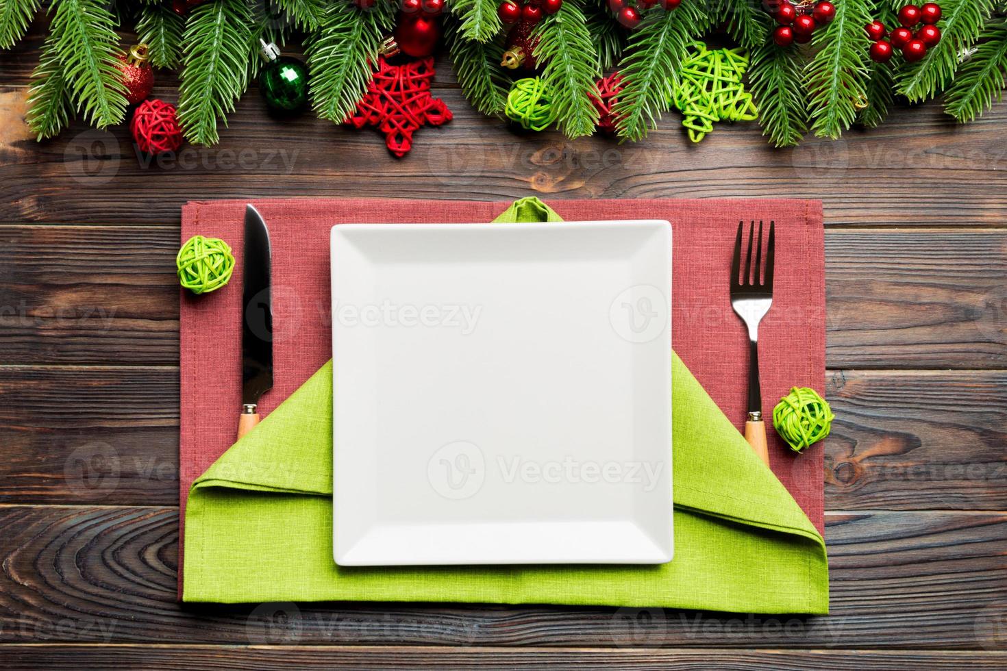 Top view of New Year dinner on festive wooden background. Composition of plate, fork, knife, fir tree and decorations. Merry Christmas concept photo