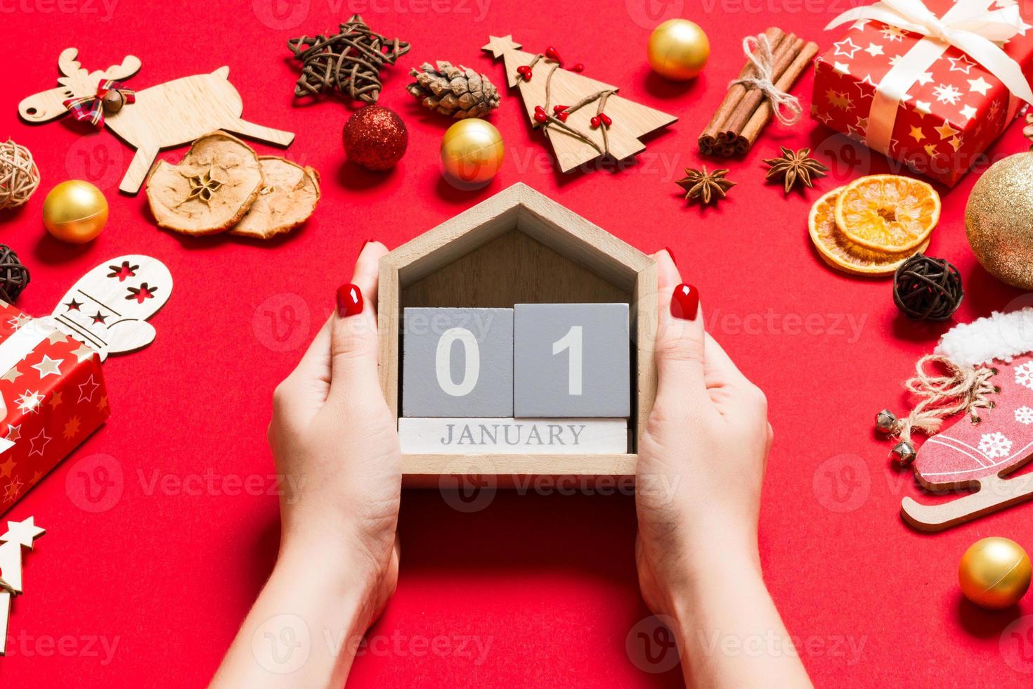 Top view of female hands holding calendar on red background. The first of January. Holiday decorations. New Year concept photo