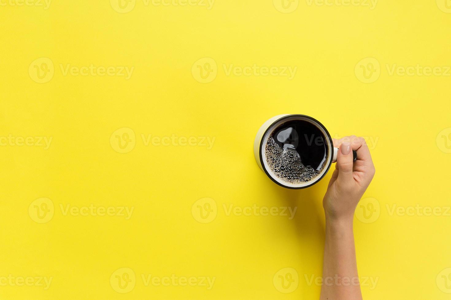 female arms hold mug of coffee on yellow background. top view with cope space photo