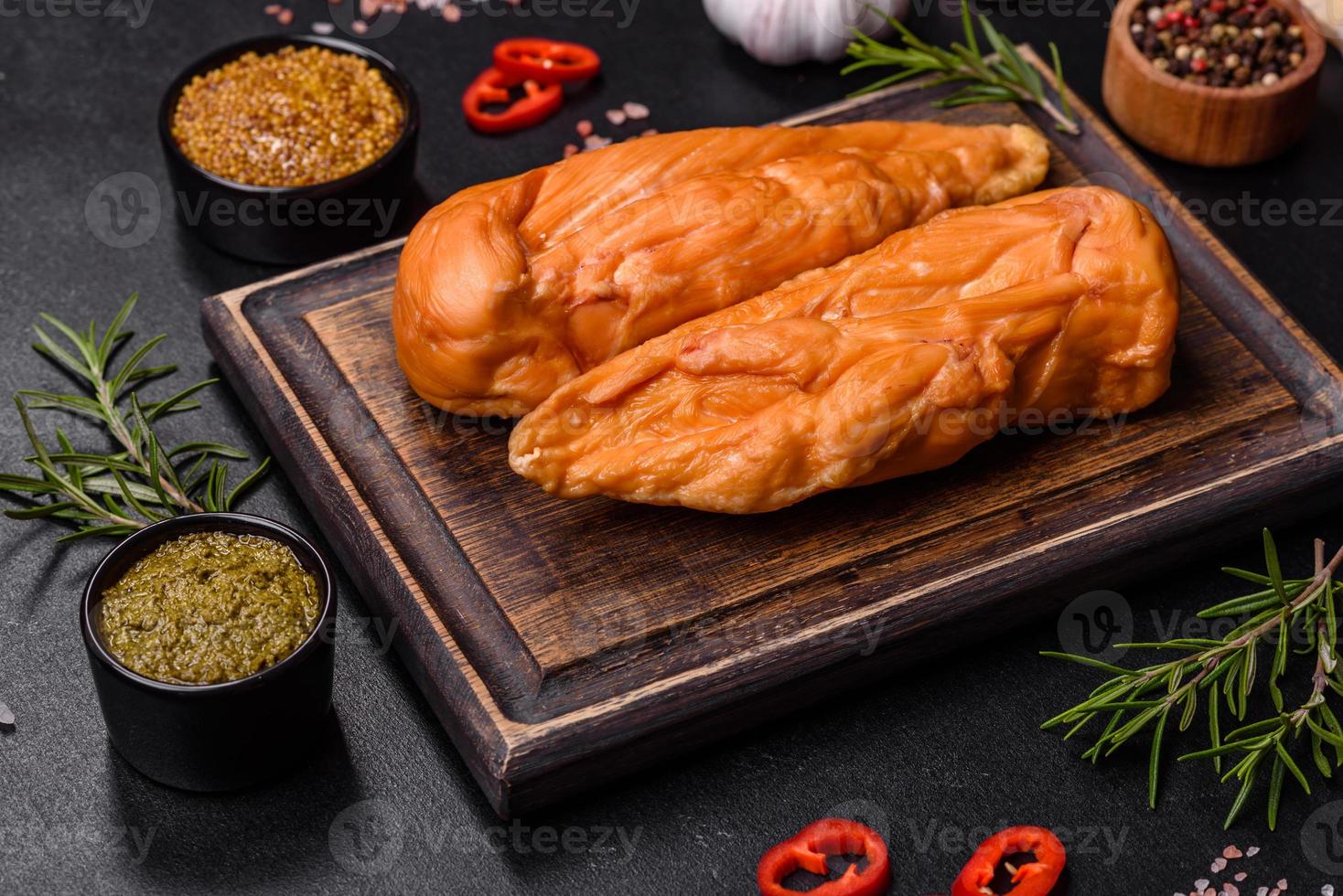 Tasty smoked fillet of chicken breast with spices and herbs on a wooden cutting board photo