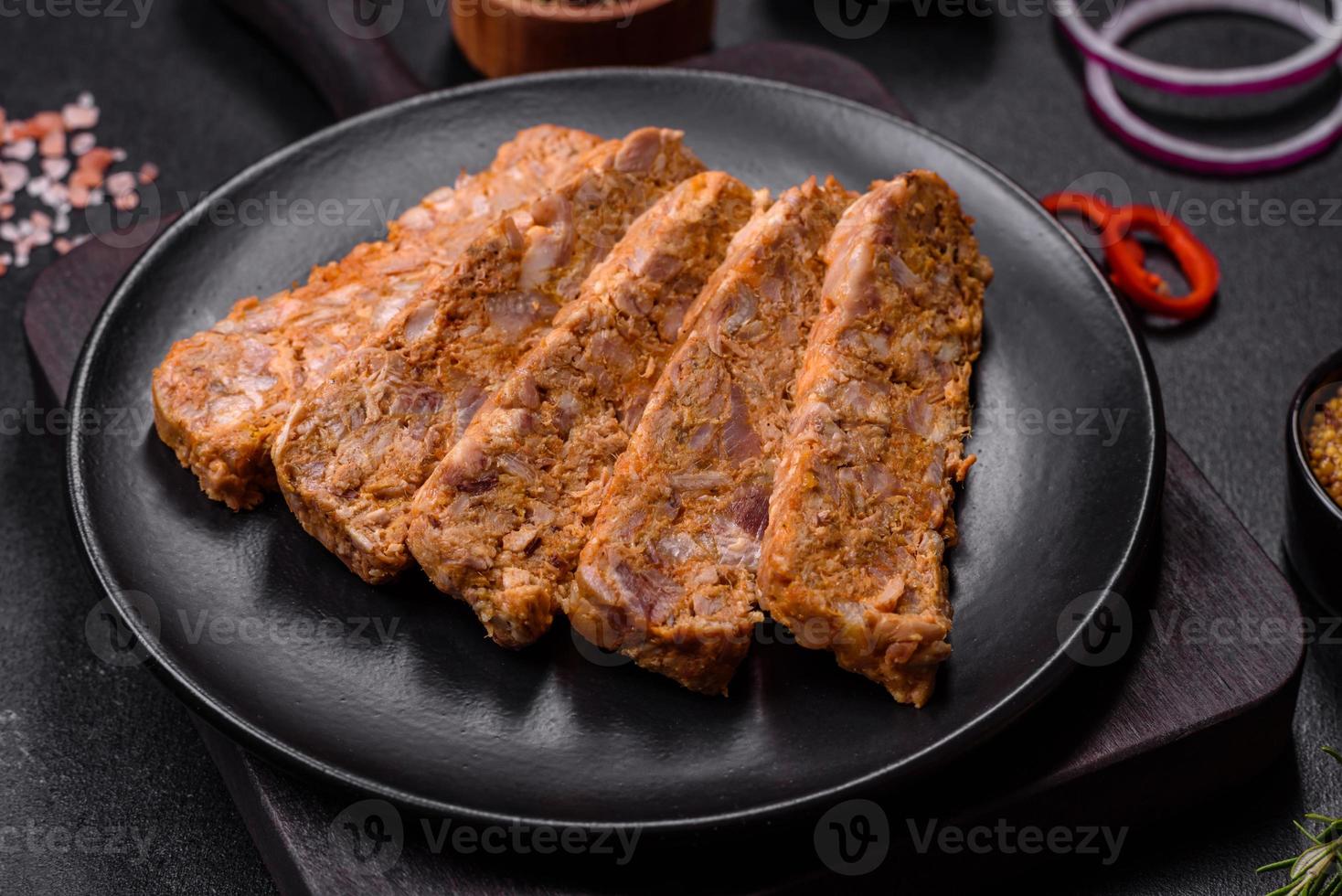 Tasty meat brawn or roll on a wooden cutting board with spices and herbs photo