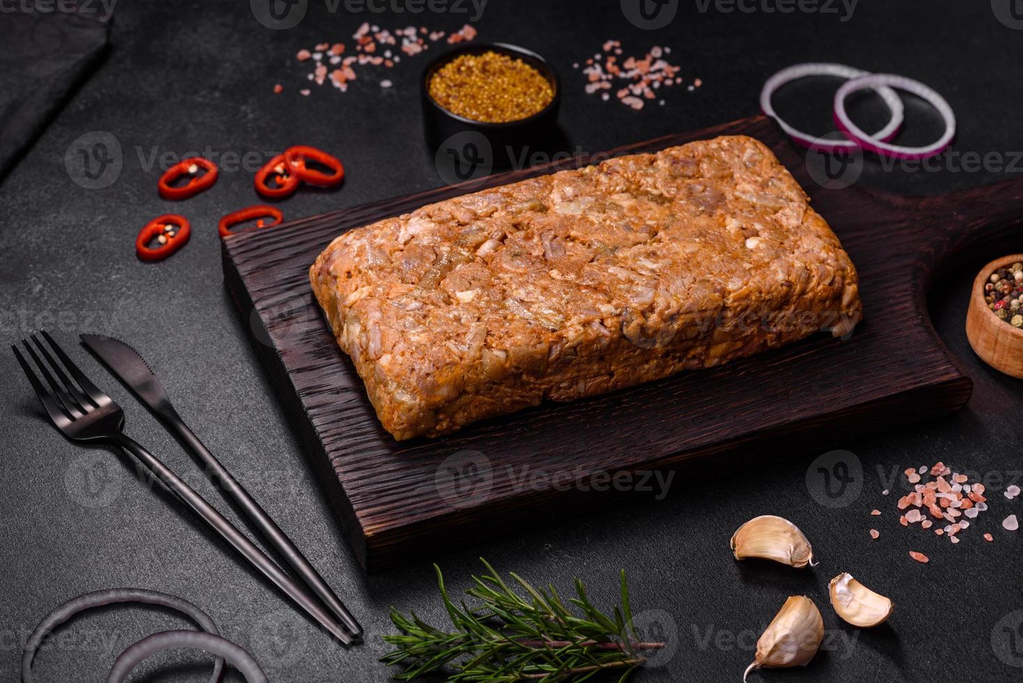 Tasty meat brawn or roll on a wooden cutting board with spices and herbs photo