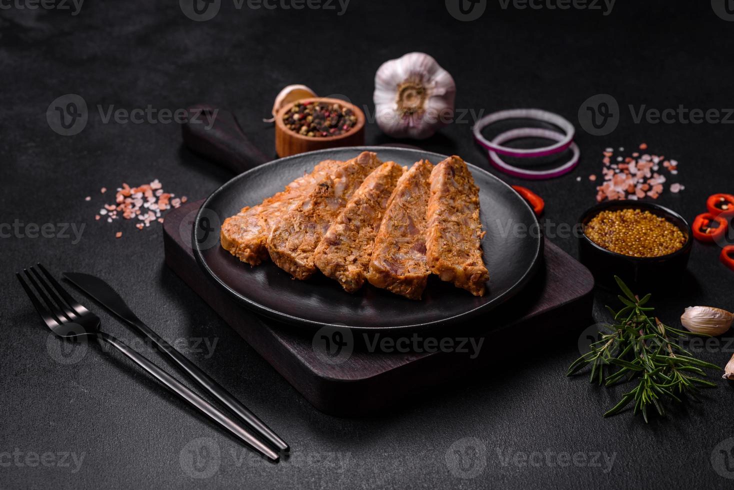 Tasty meat brawn or roll on a wooden cutting board with spices and herbs photo