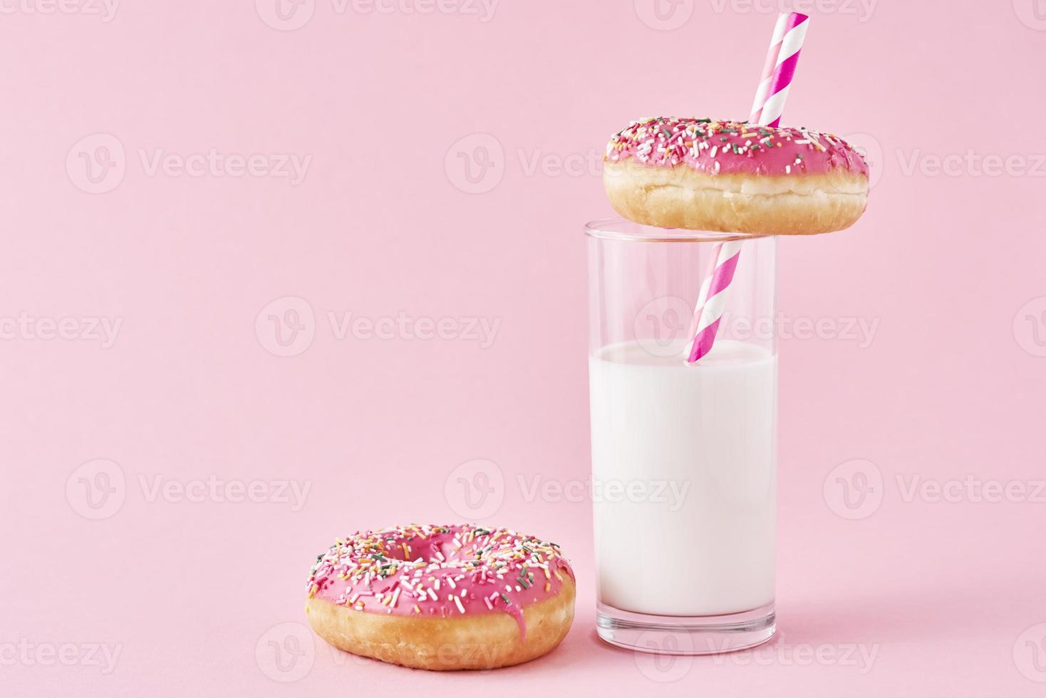 Donuts decorated with icing and sprinkle and glass of milk on a pink background photo