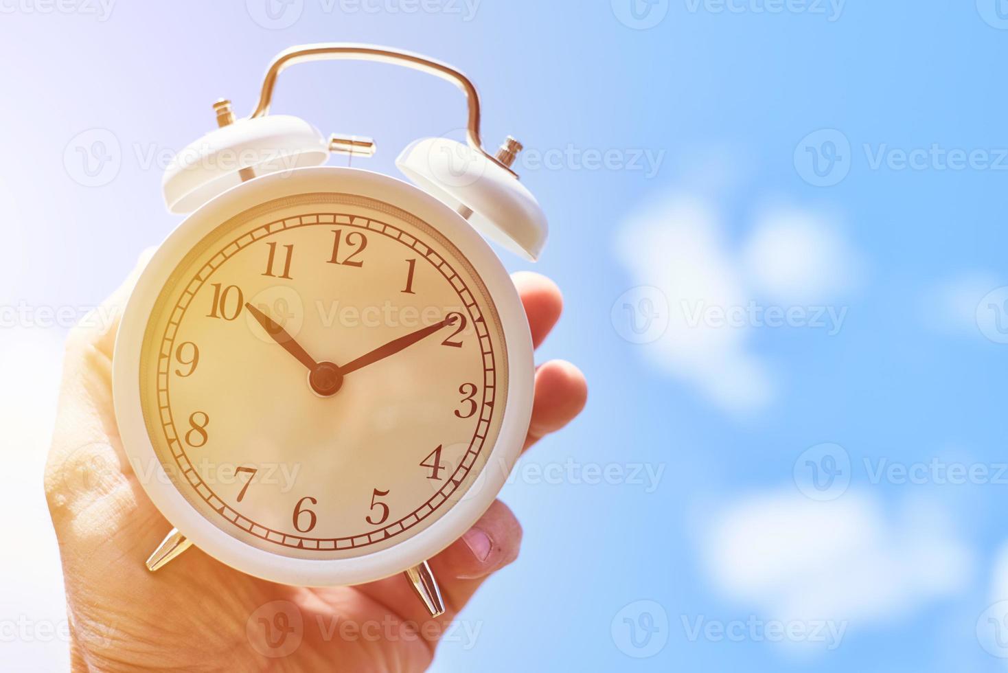 Hand hold vintage alarm clock against blue sky. Deadline and change time concept photo