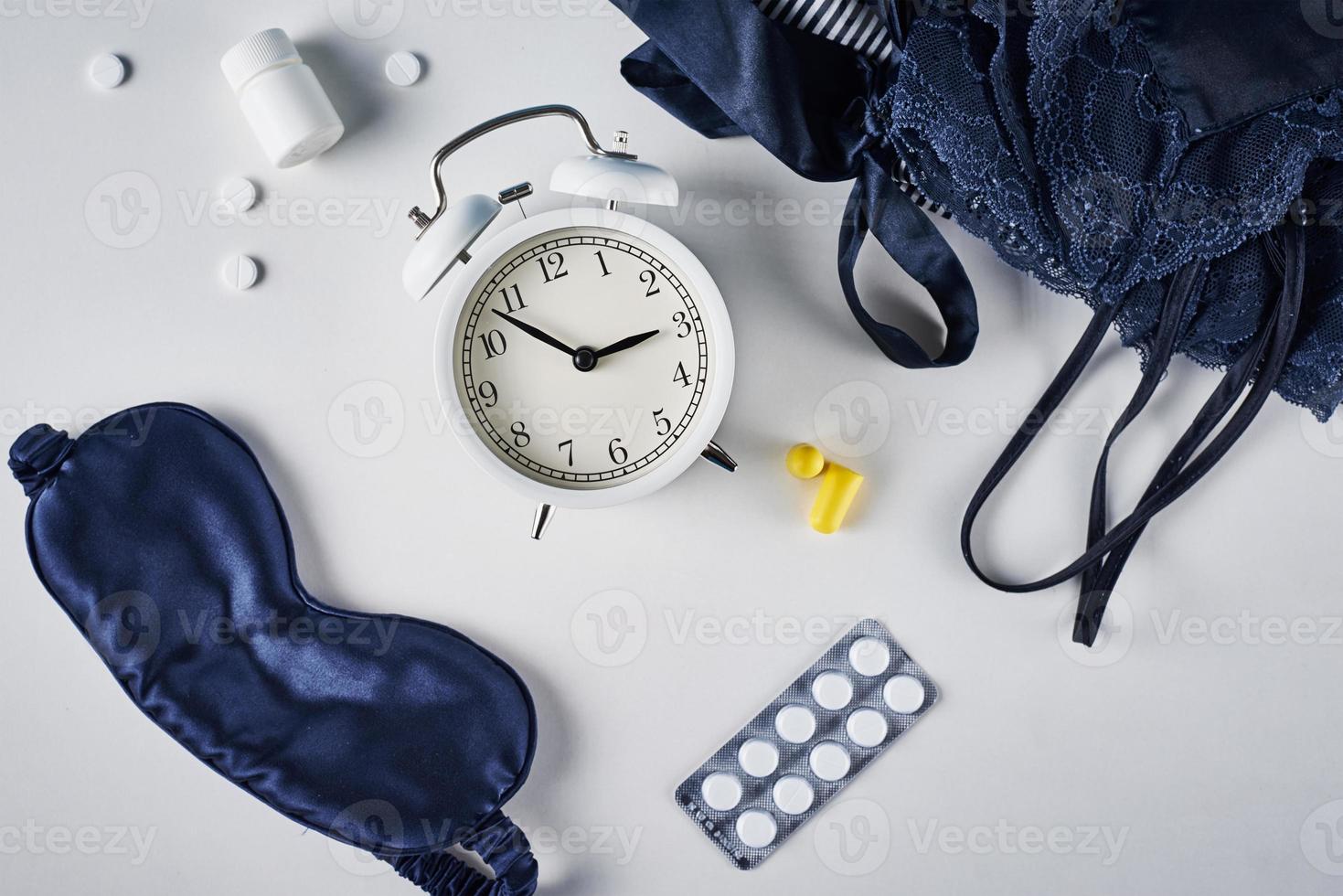 Alarm clock, sleeping mask, ear plugs and pills on a white background