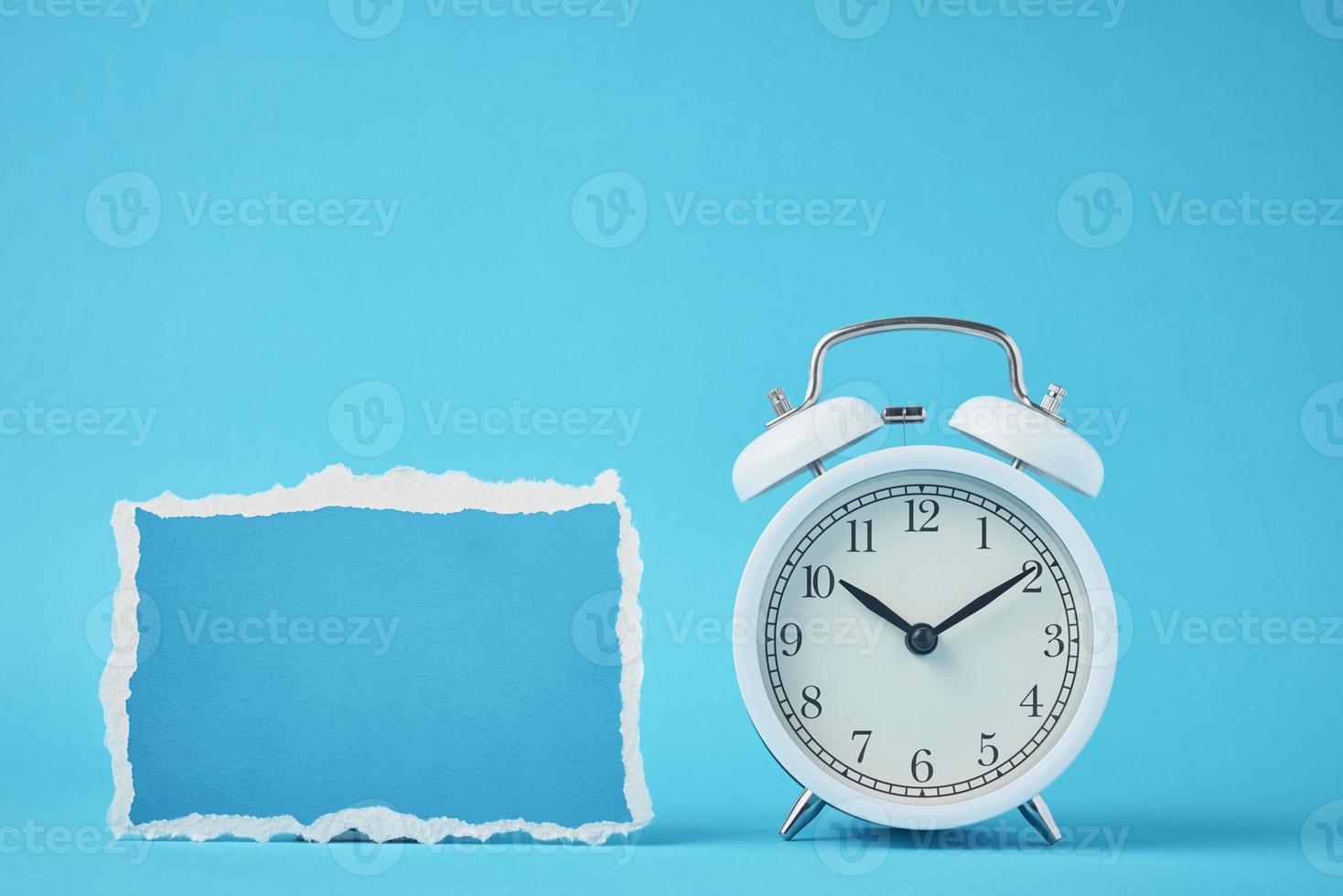 Alarm clock with bells and empty torn paper sheet on the blue background photo