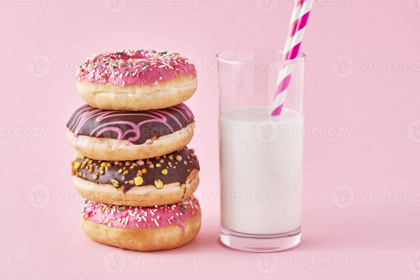 Stack of colorful donuts decorated and glass of milk on a pink background photo