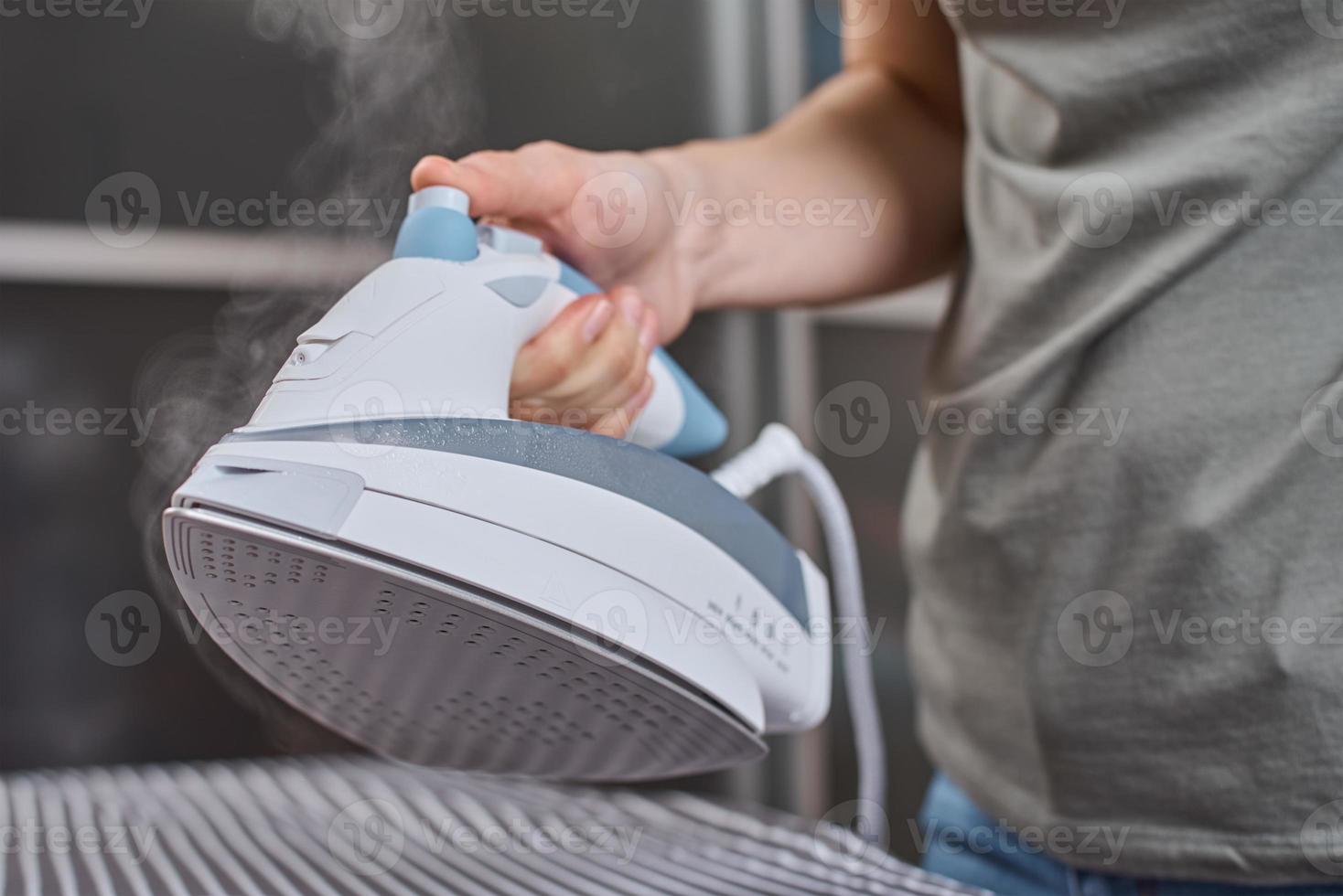 Steam boost on the modern iron. Woman ironing clothes with modern iron photo