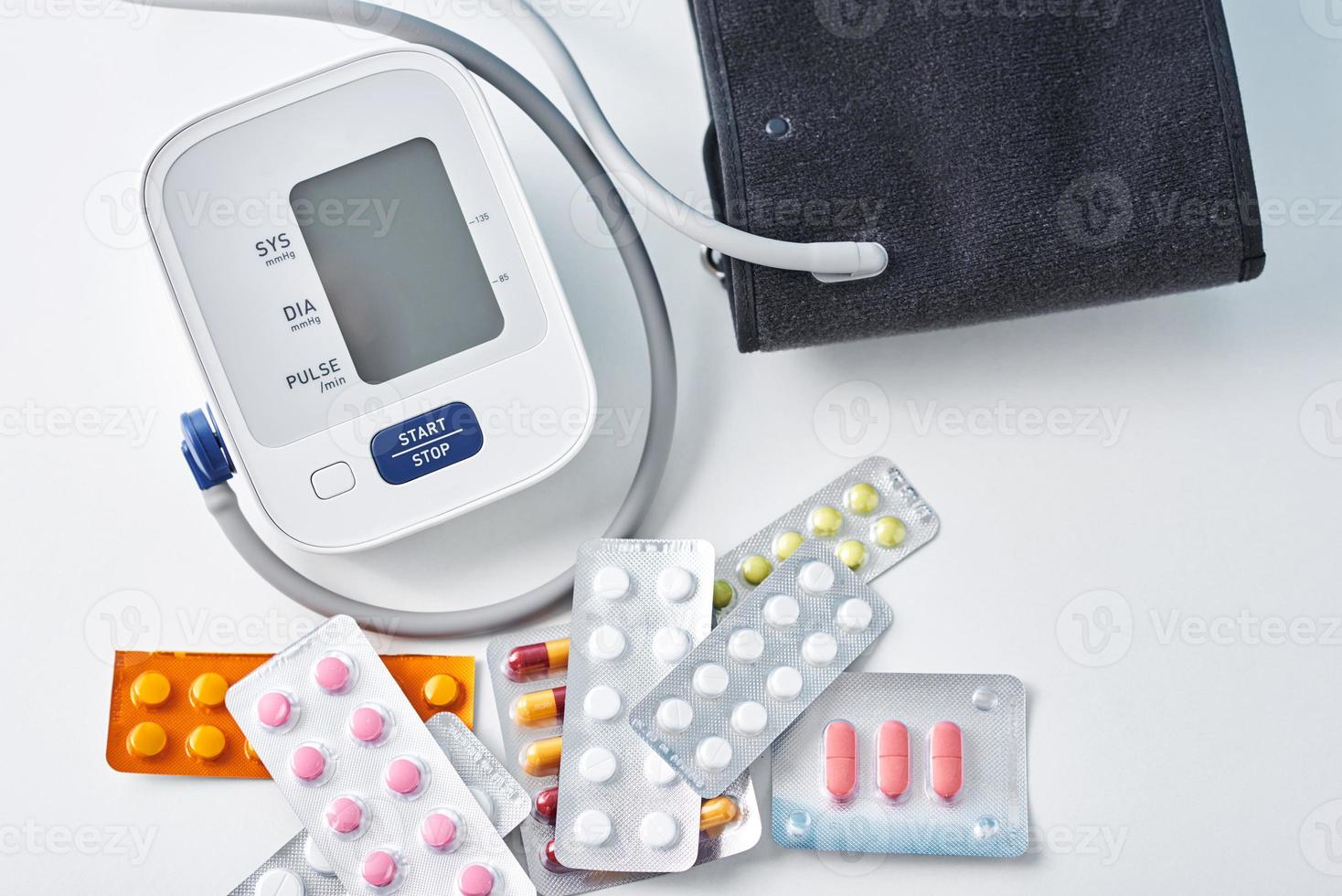 Digital blood pressure monitor and medical pills on the white table photo