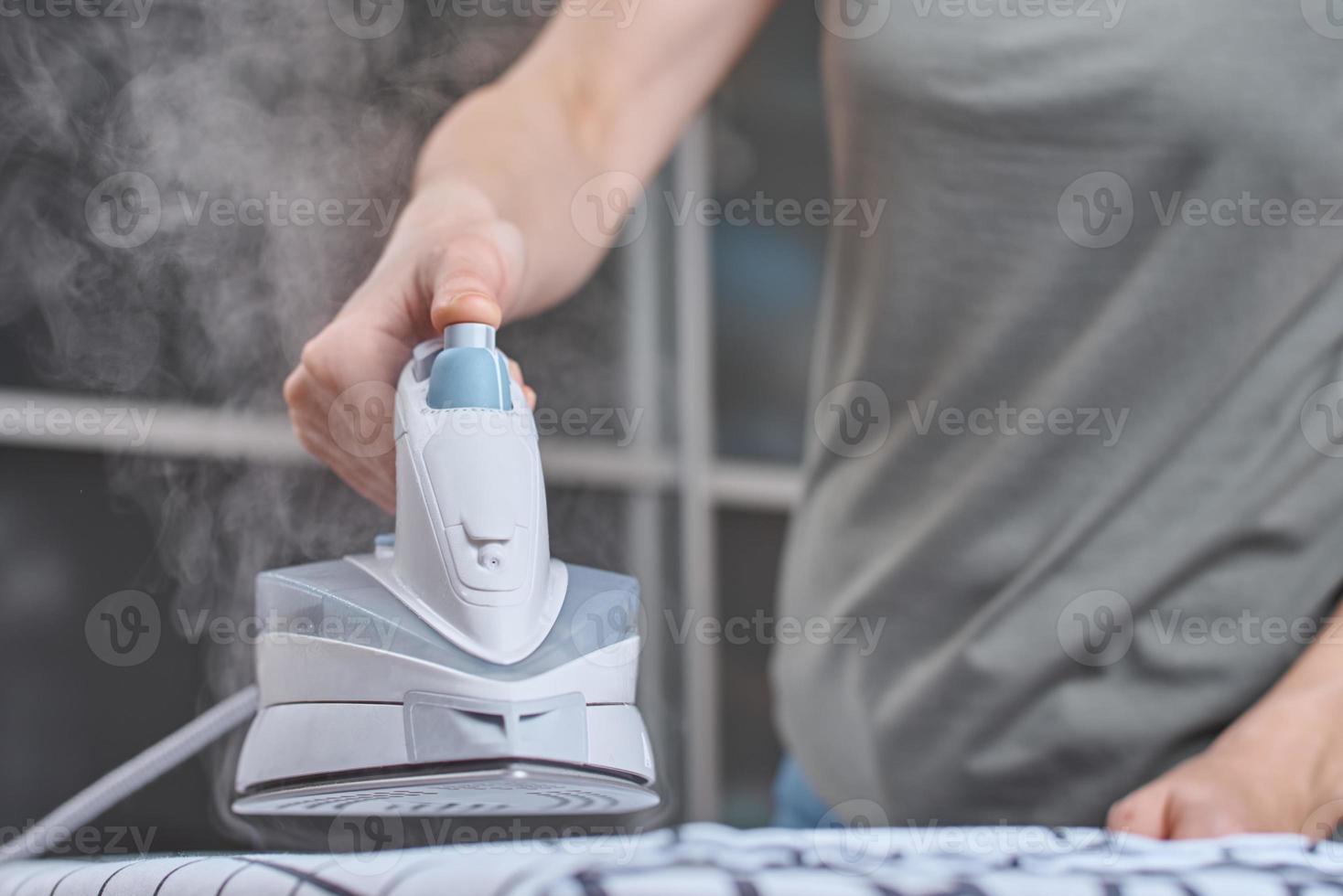 golpe de vapor en la plancha moderna. mujer planchando ropa con plancha moderna foto