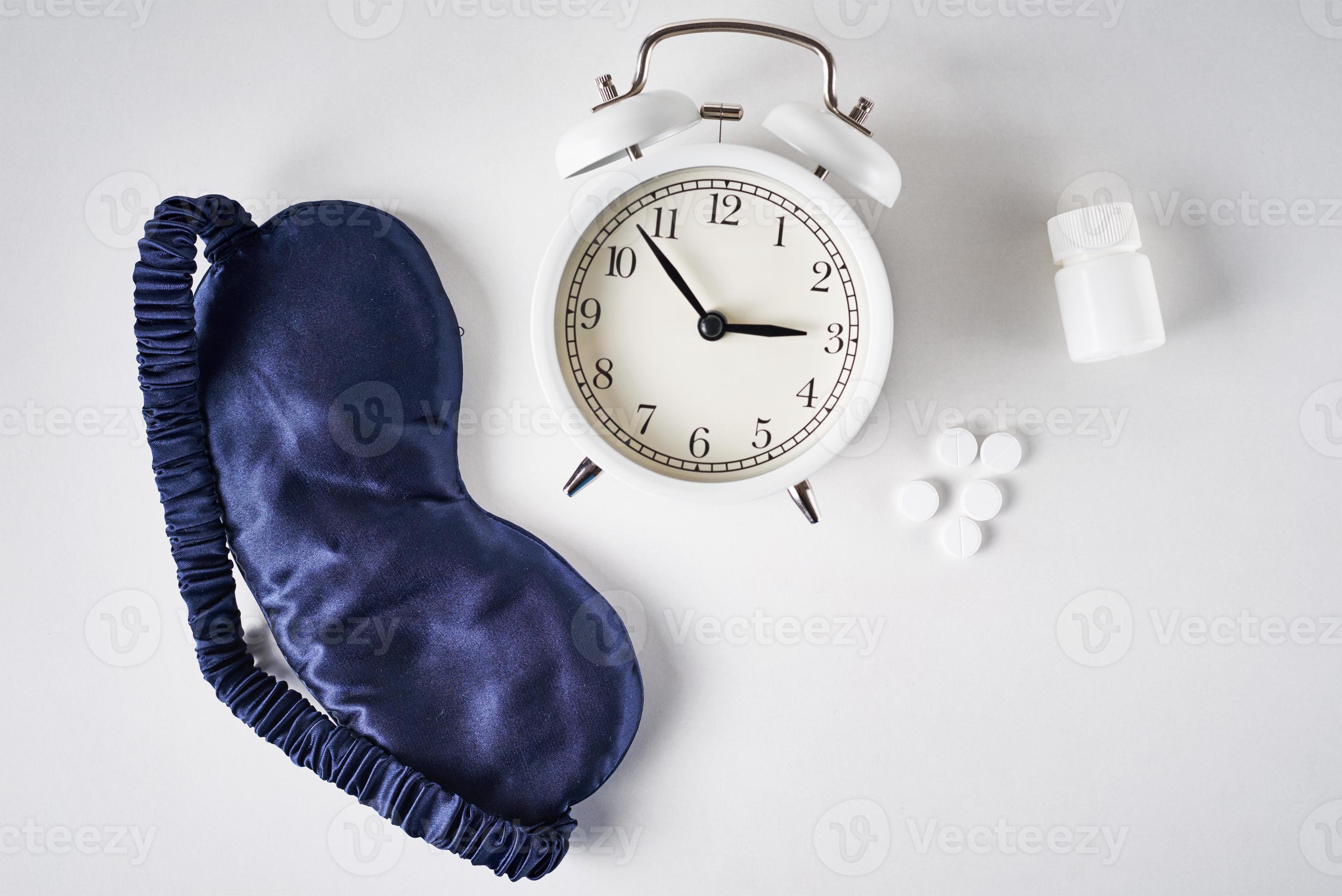Alarm clock, sleeping mask, ear plugs and pills on a white background