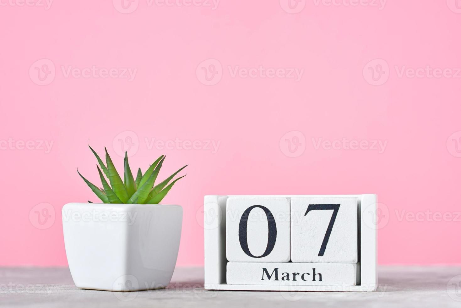 calendario de bloques de madera con fecha 7 de marzo y planta en el fondo rosa foto