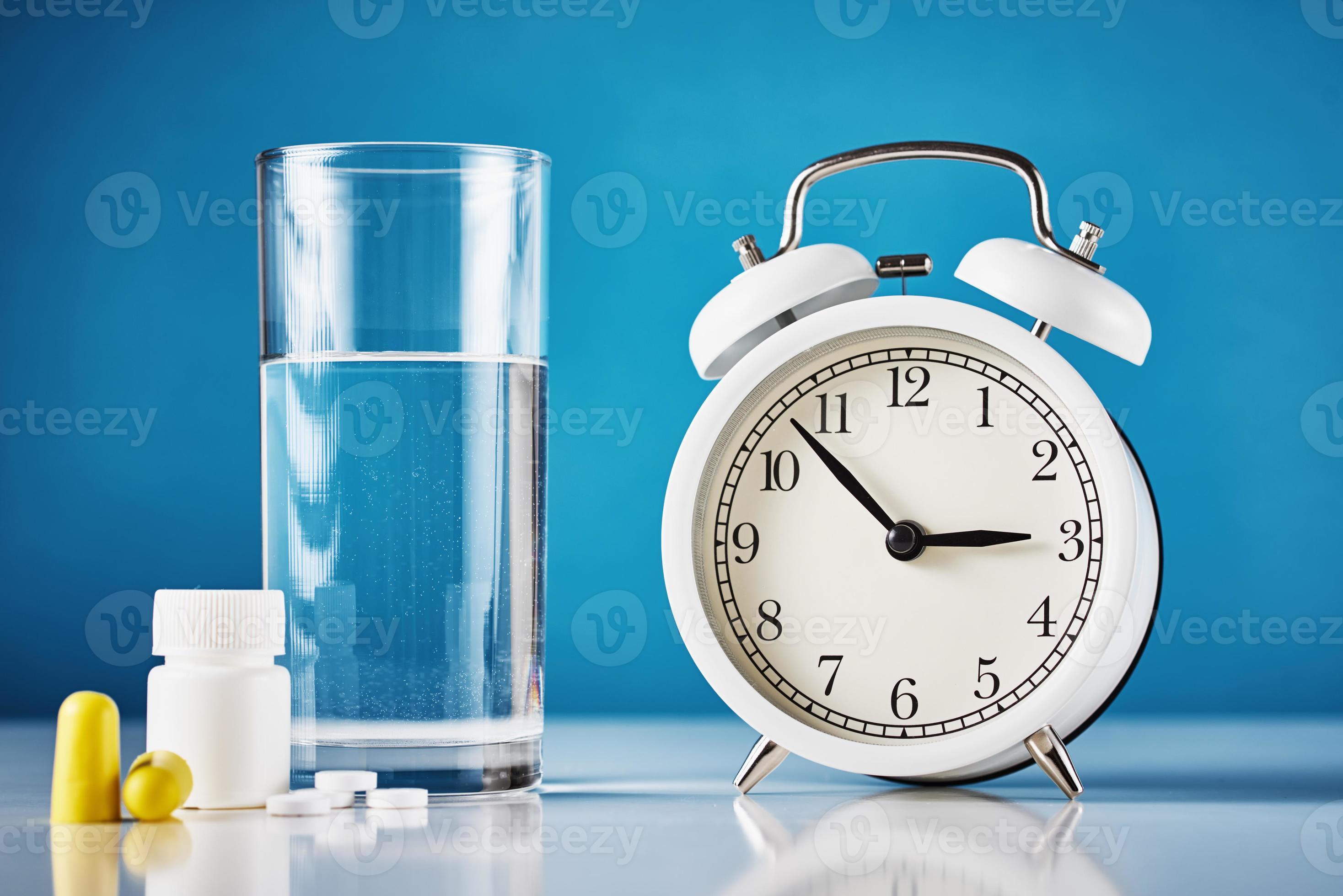 Alarm clock, glass of water, ear plugs and pills on the blue background