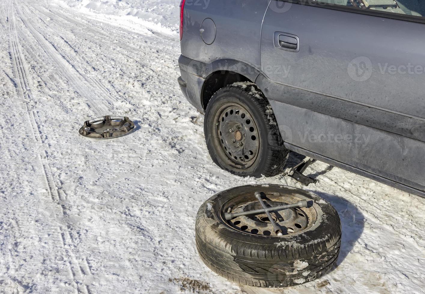 changing a flat tire in the winter snow with backup photo