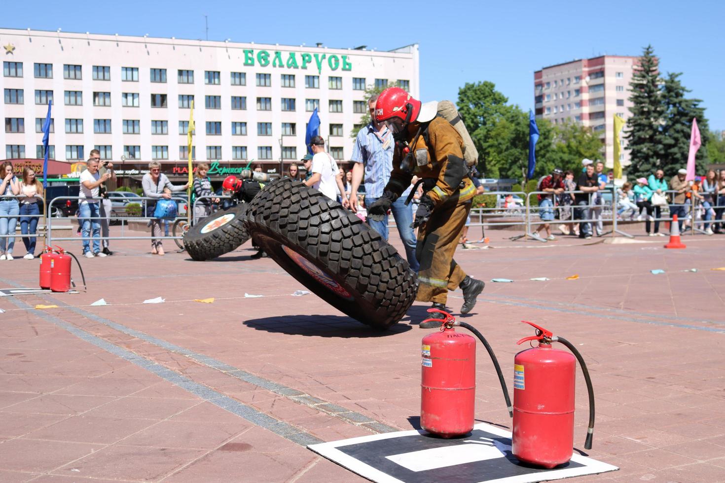 un bombero con traje ignífugo y casco corre y gira una gran rueda de goma en una competencia de extinción de incendios, bielorrusia, minsk, 08.08.2018 foto
