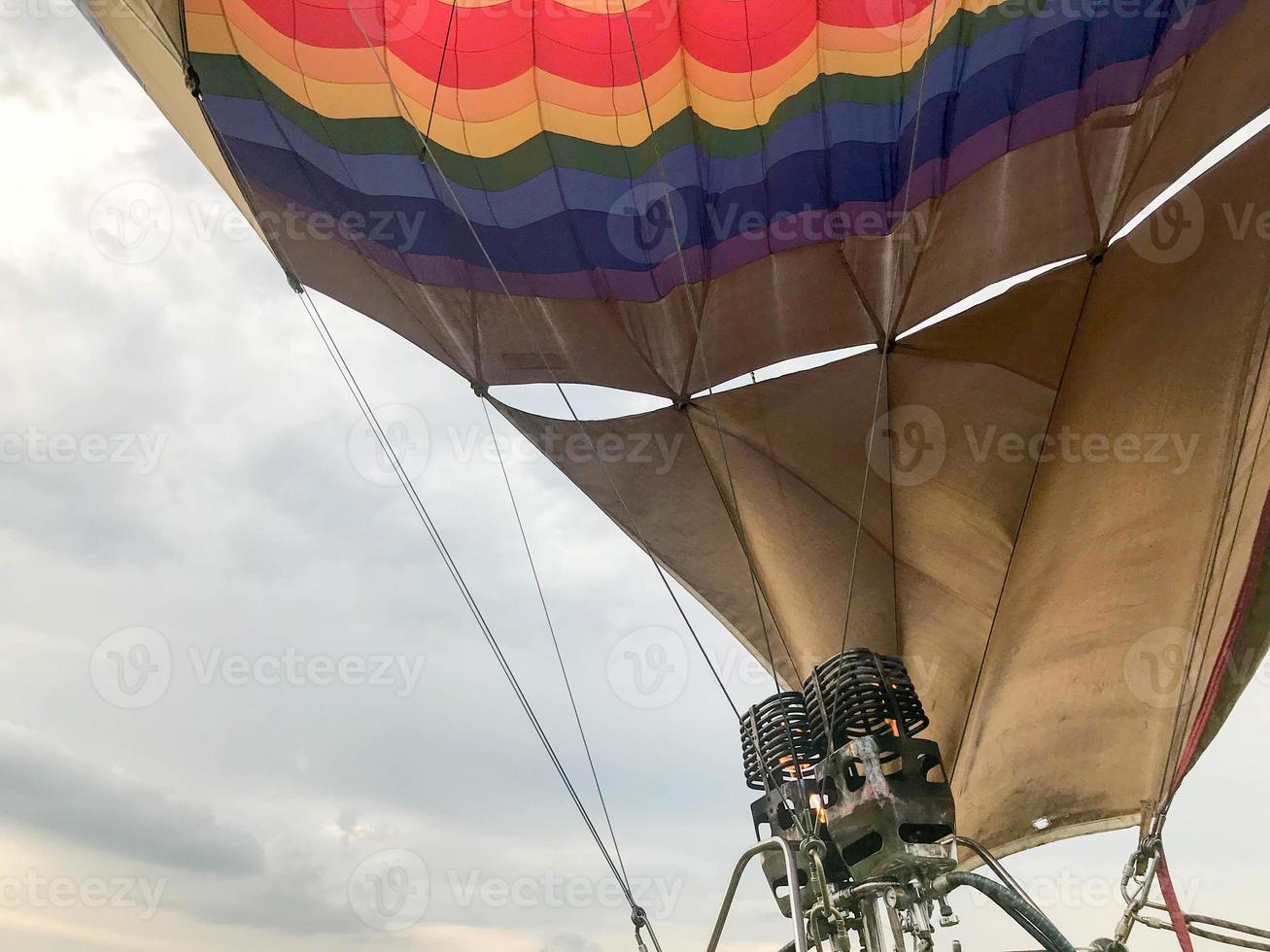 Large powerful metal iron burners, thermal hair dryers with a fire to heat hot air in a large multi-colored bright round rainbow colored striped flying balloon. The background photo