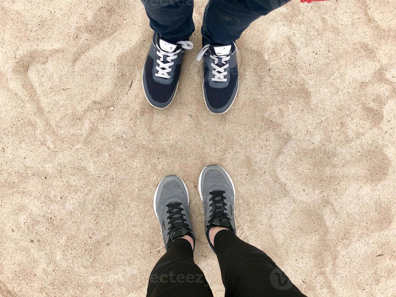 Two pairs of legs in sneakers shoes stand opposite each other against the background of natural loose yellow golden beautiful warm beach sand photo