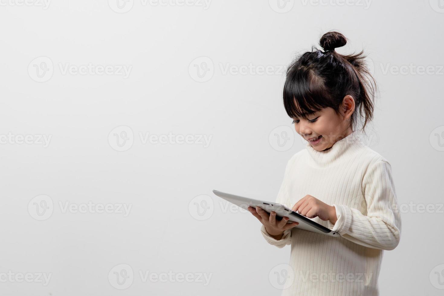 Asian little girl holding and using the digital tablet on white studio background, free copy space photo