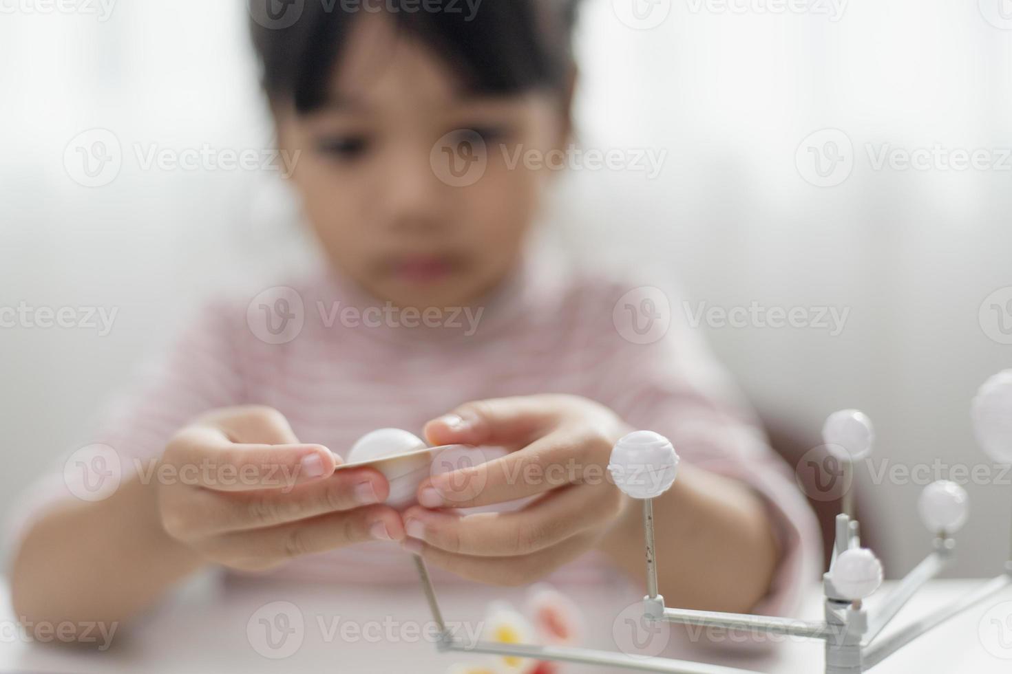 Asian Little girl studies the solar system in geography class. looking at the scale model of planets photo