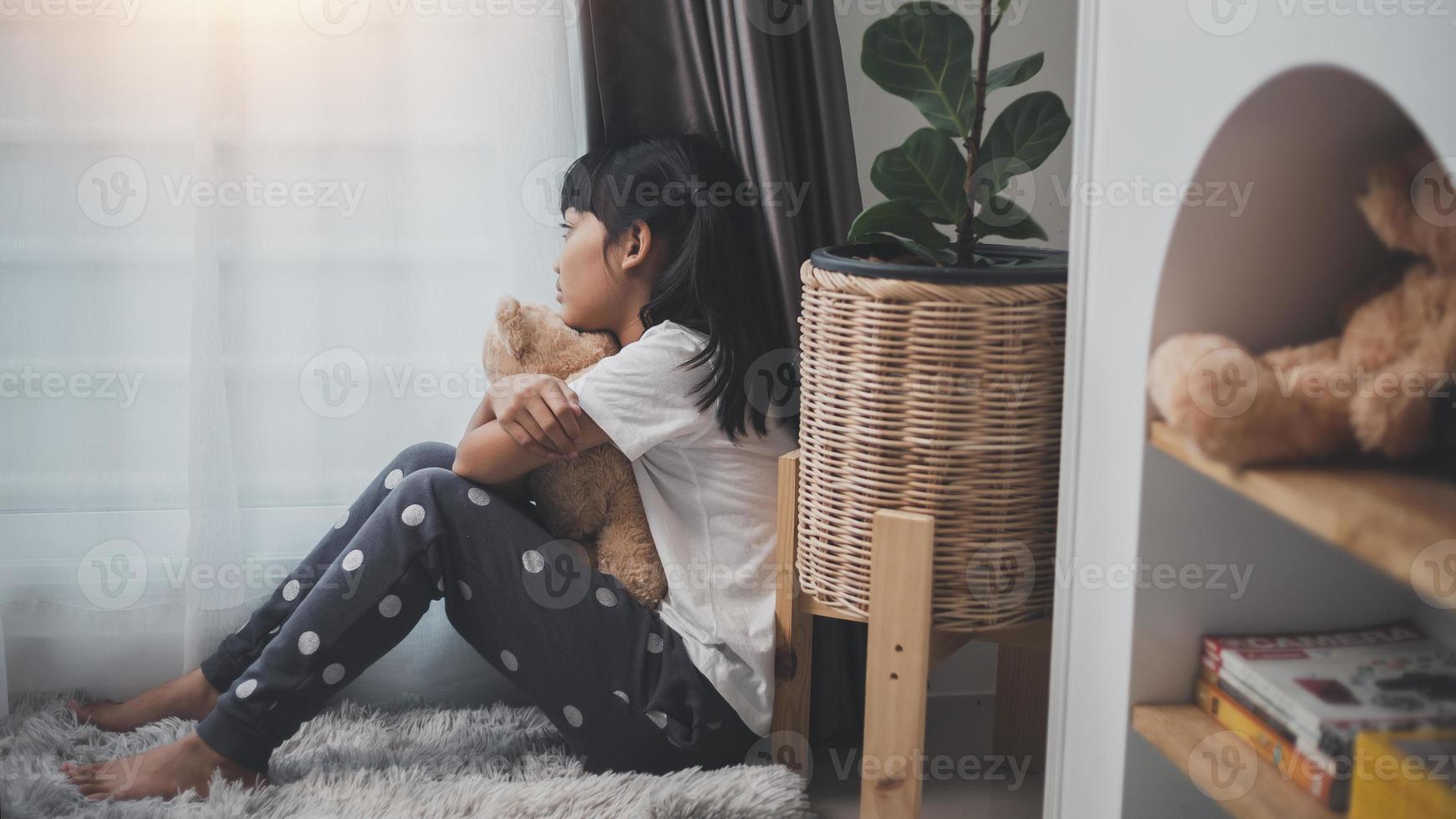 Close up lonely little girl hugging toy, sitting at home alone, upset unhappy child waiting for parents, thinking about problems, bad relationship in family, psychological trauma photo