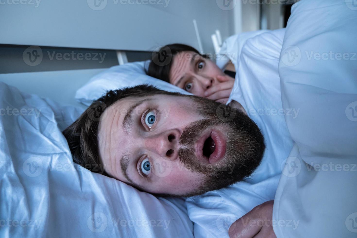 Man had a terrible nightmare, he woke up in horror, opened mouth and made big eyes, a frightened woman looks at him from behind. photo