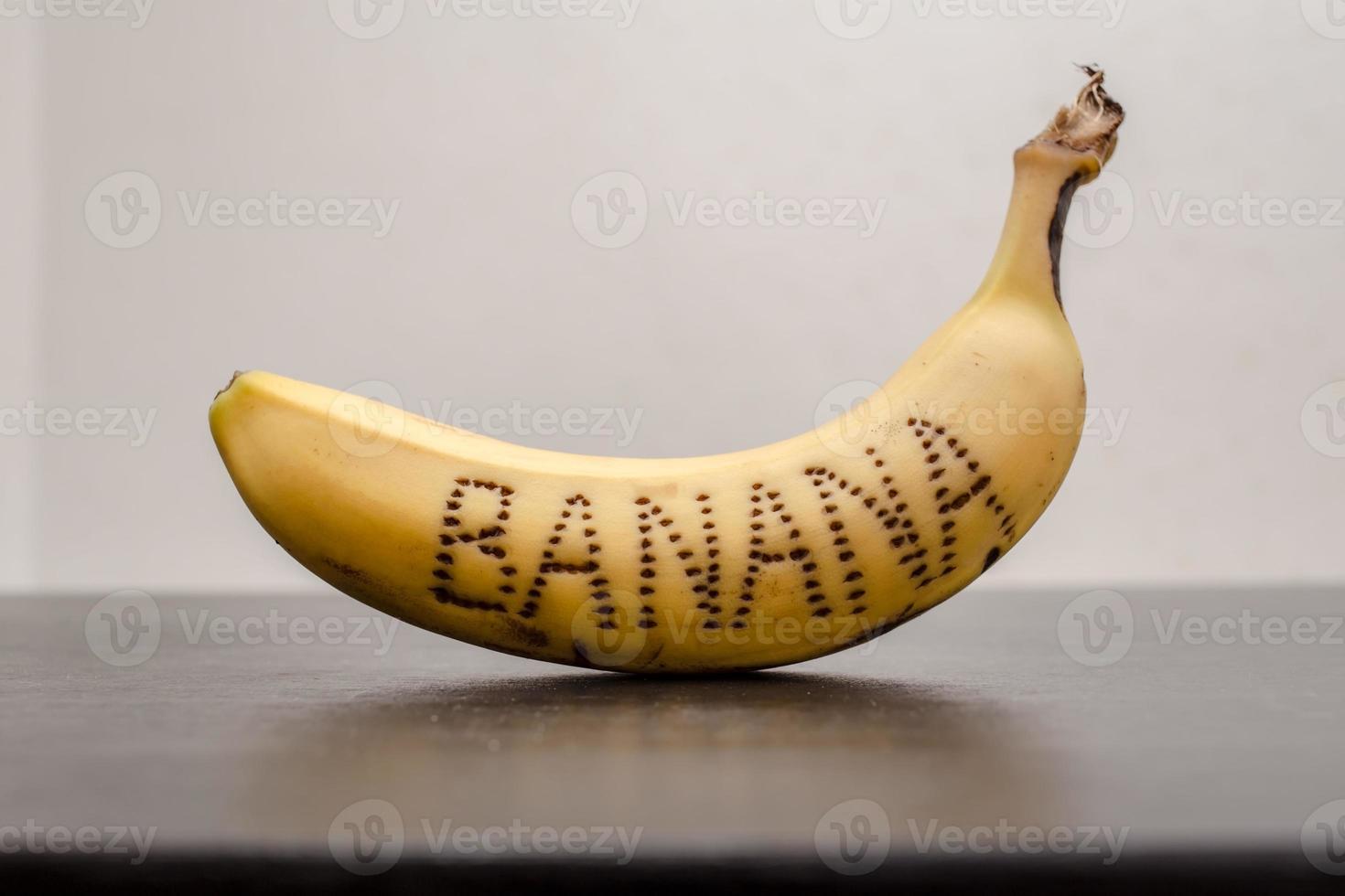 Banana with handwritten inscription on the peel, on a black table, on a white background. Creative idea. photo
