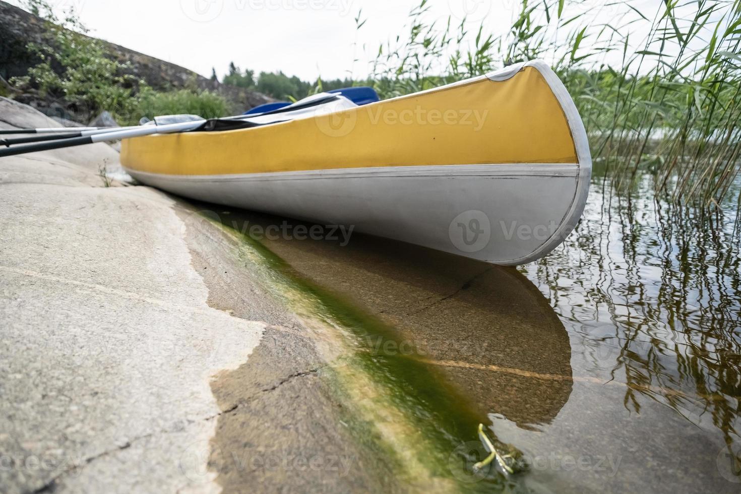 kayak con remos estacionado en la orilla rocosa del lago, en el hermoso paisaje. descanso activo. foto