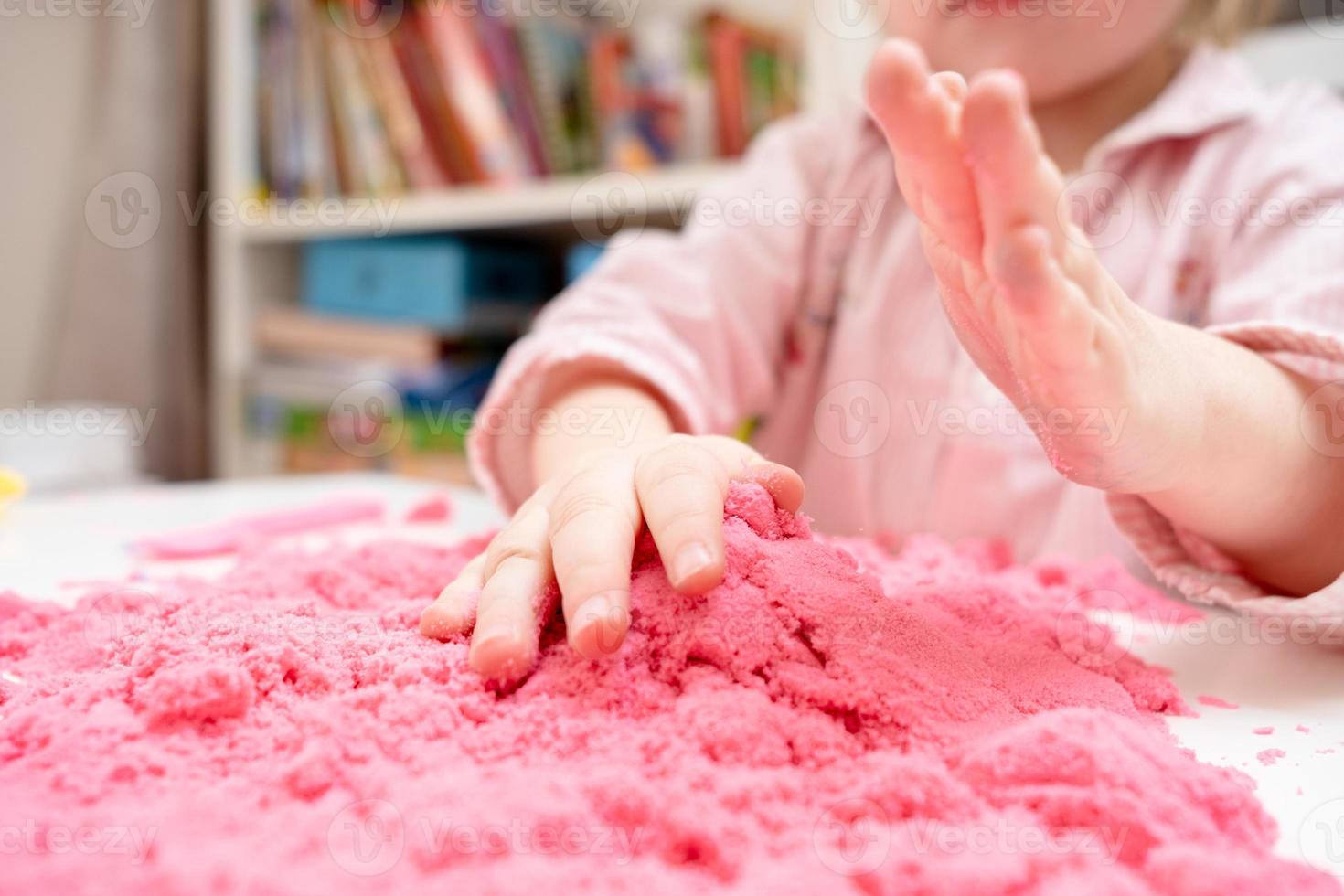 Enthusiastic child is playing with pink kinetic sand. Concept of developing fine motor skills and creative imagination in children. photo