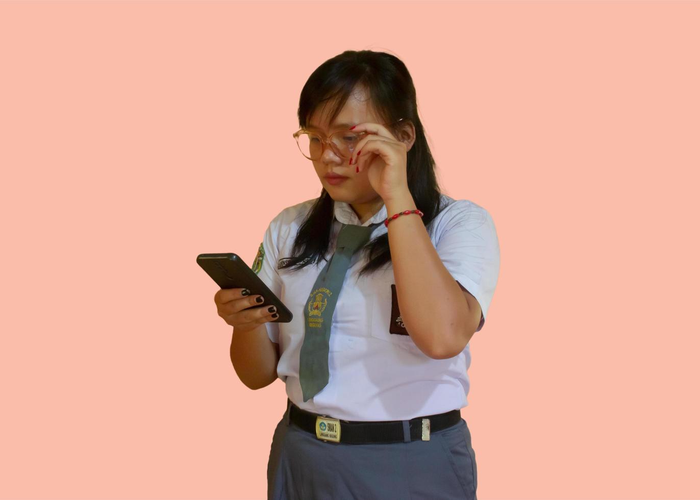 siswa sma o estudiante de secundaria en indonesia vistiendo el típico uniforme gris blanco mientras posa sosteniendo teléfonos inteligentes. foto