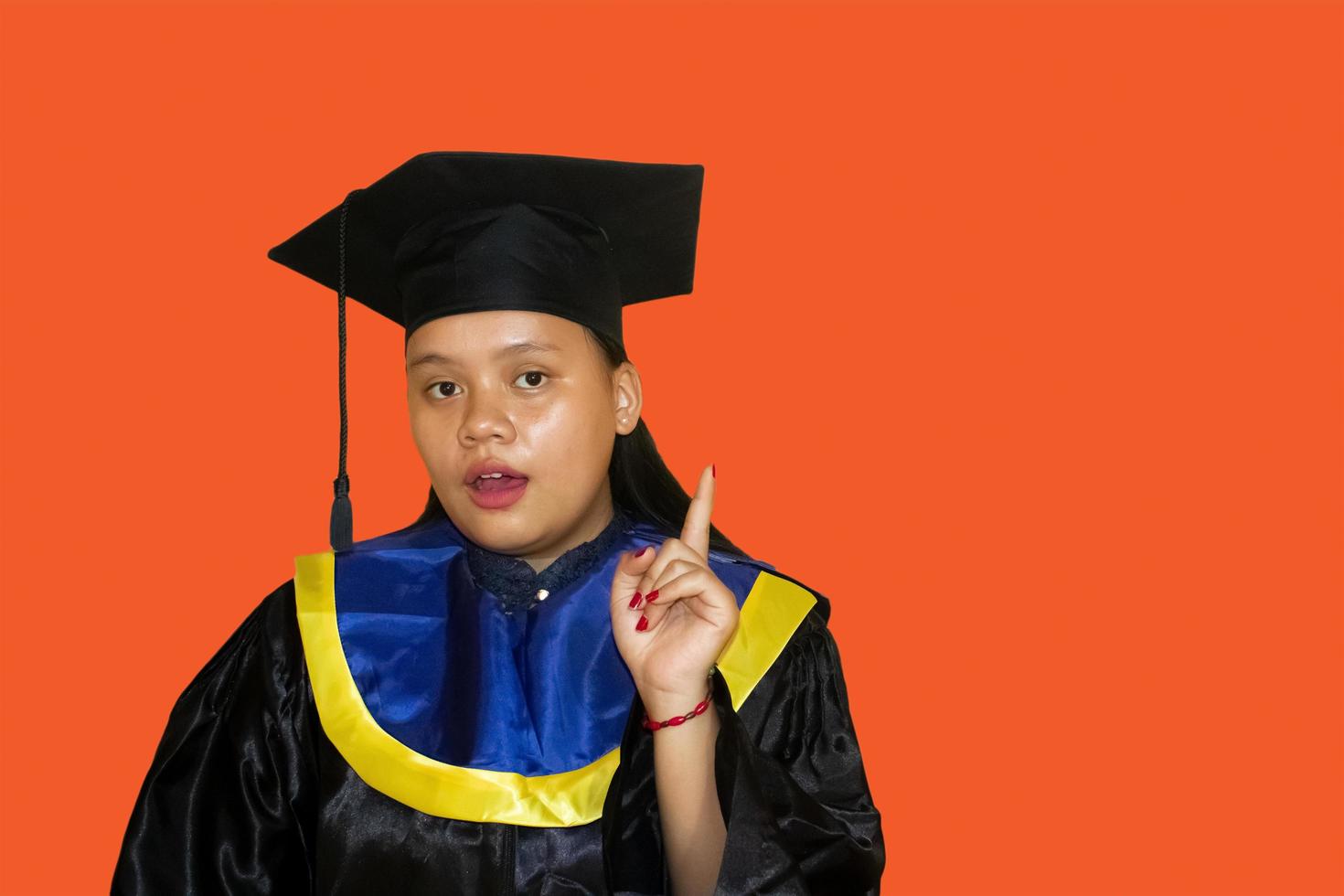 Apuntando hacia Arriba. una joven estudiante sonriente con un vestido de graduación. concepto de educación, graduación y vida estudiantil. tiene una idea. foto