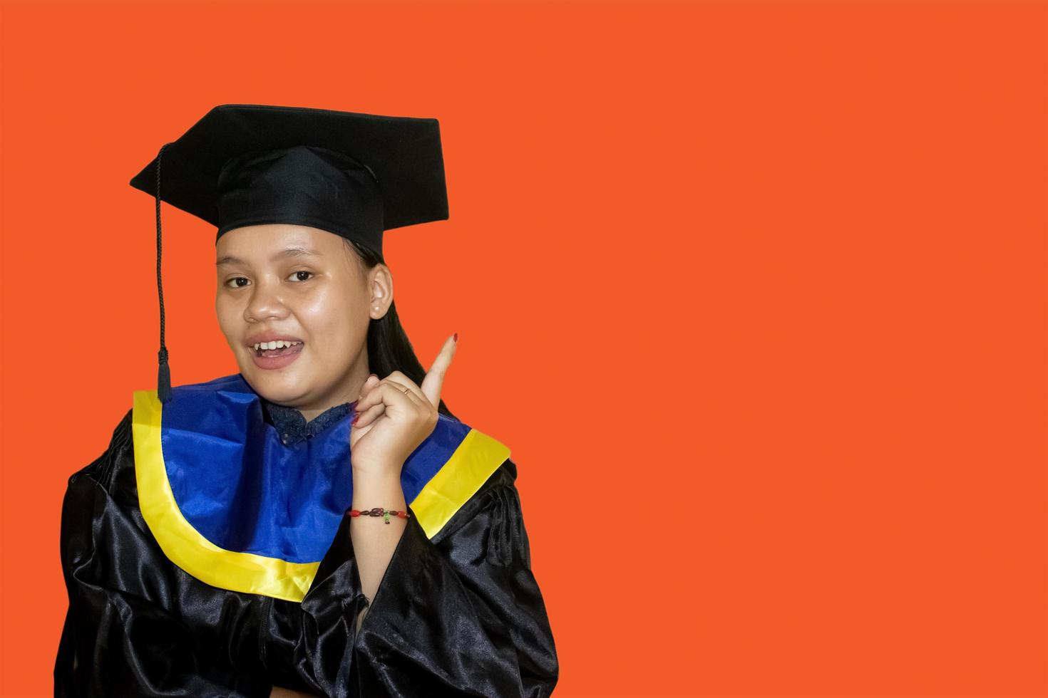 Apuntando hacia Arriba. una joven estudiante sonriente con un vestido de graduación. concepto de educación, graduación y vida estudiantil. tiene una idea. foto