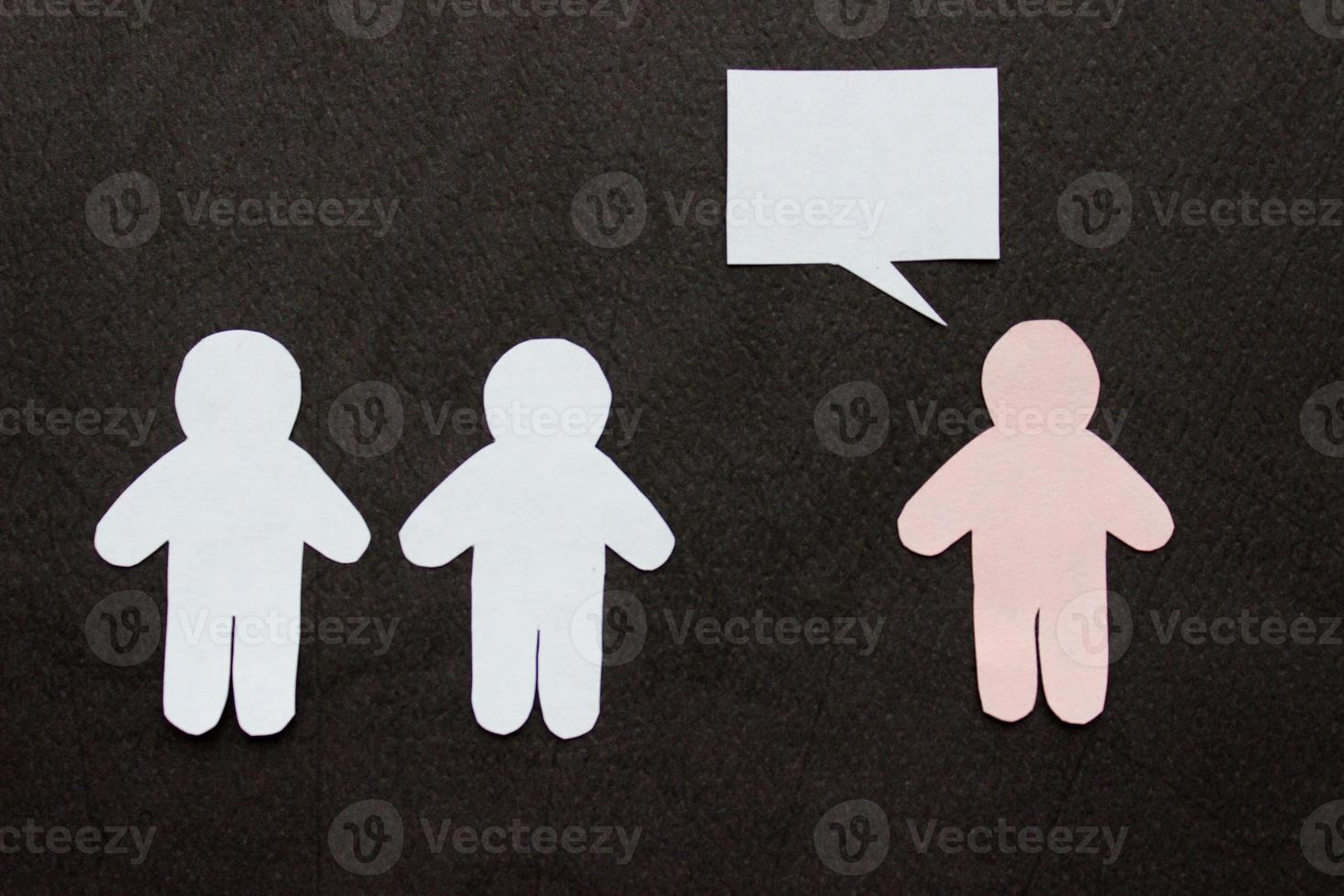 Silhouettes of people cut from white and pink paper on a black background. Two people stands in front of one person, pink figure with speech-bubble. Communication, leadership, teamwork concept photo