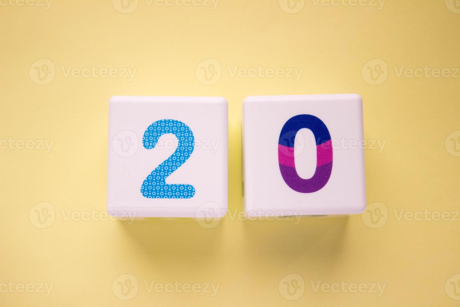 Close-up photo of a white plastic cube with a violet number 20 on a yellow background. Object in the center of the photo