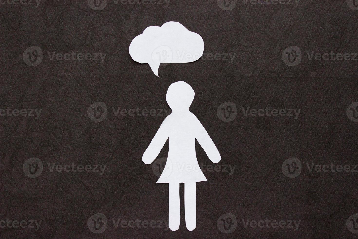 The silhouette of a woman in a dress made of white paper, cut by hand. With speech-bubble in the center of the photo on black background