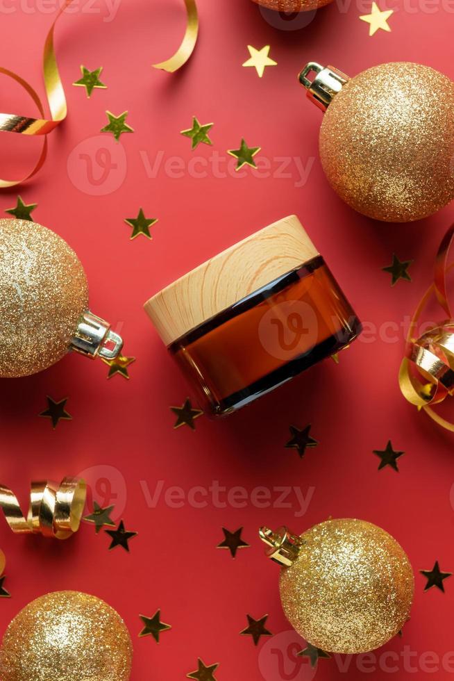 Creative new year and christmas presentation of cosmetics packaging. Amber glass unbranded cream jar with glitter gold baubles, confetti on red background. Trendy mockup for you brand photo