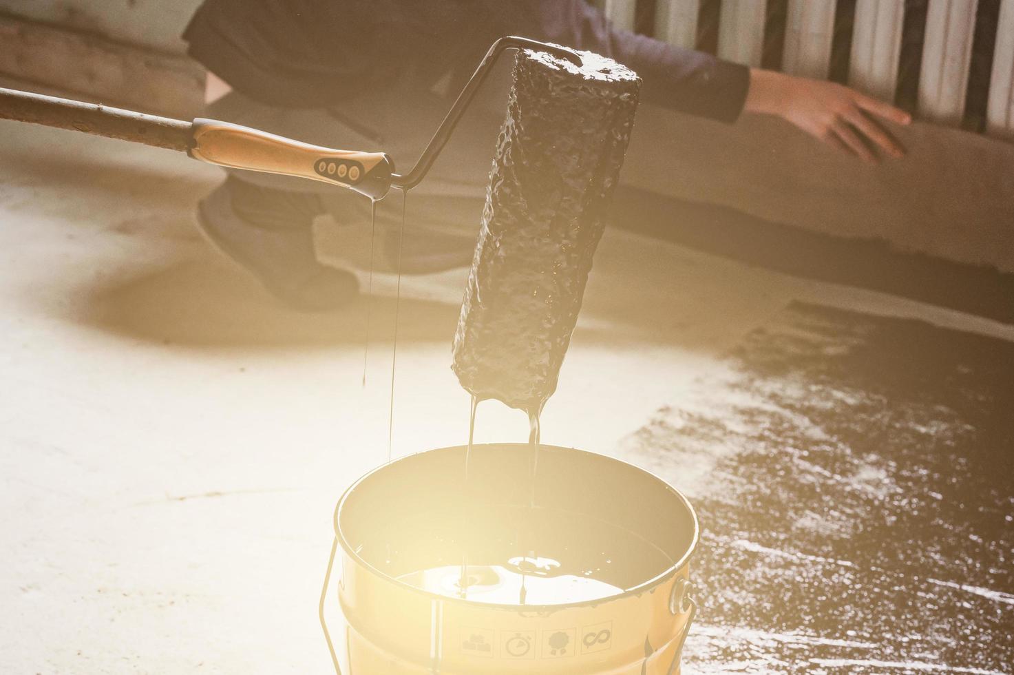 Applying hot resin to the floor for waterproofing, roller and bucket of resin. photo