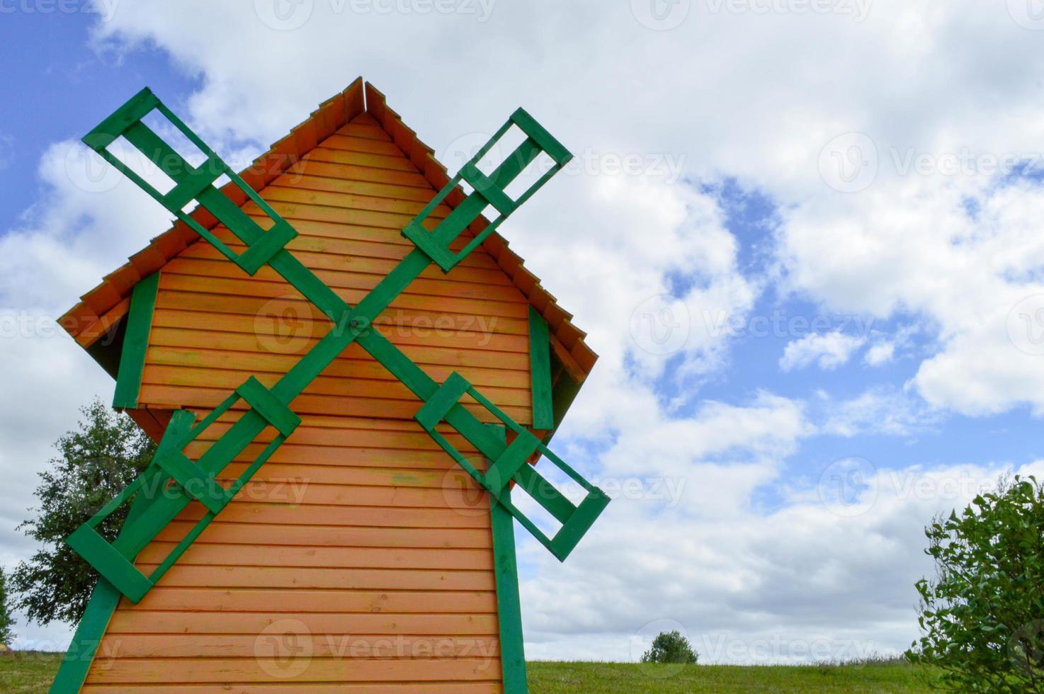 un hermoso molino de madera es un molino de viento natural rústico hecho de tablas de troncos amarillos y verdes contra un cielo azul con nubes foto