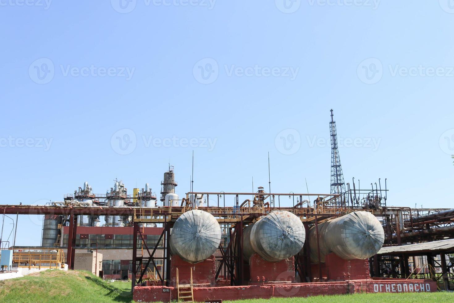 A large metallic iron pipeline trestle with pipes and wires for electricity in a petrochemical chemical refinery in the background of shell-and-tube heat exchangers and equipment photo