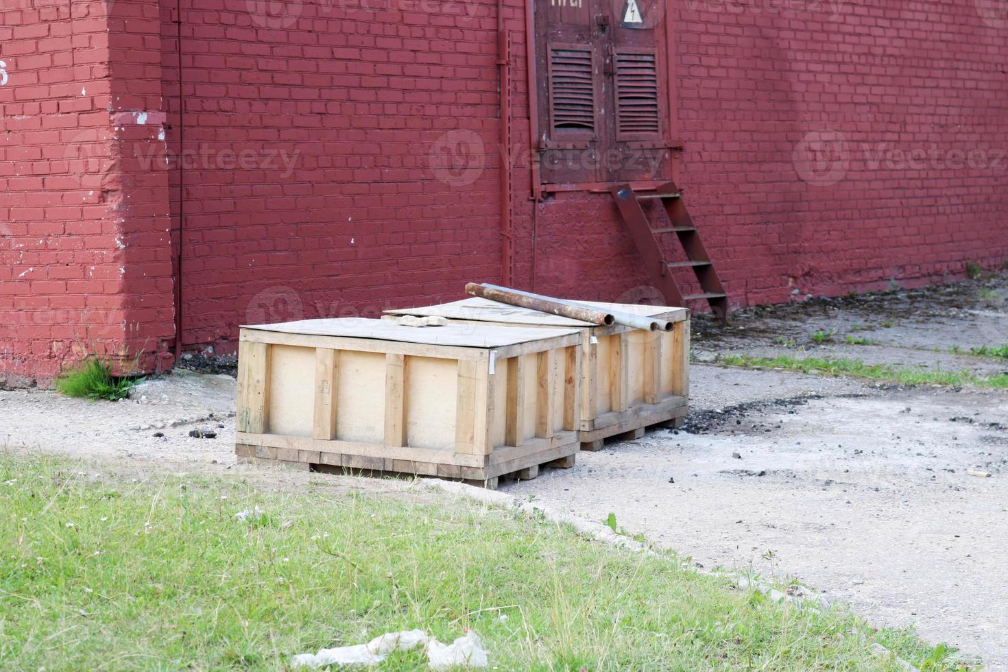 Large wooden boxes with goods stand outside in the open air in the warehouse of an industrial enterprise against a red brick wall photo